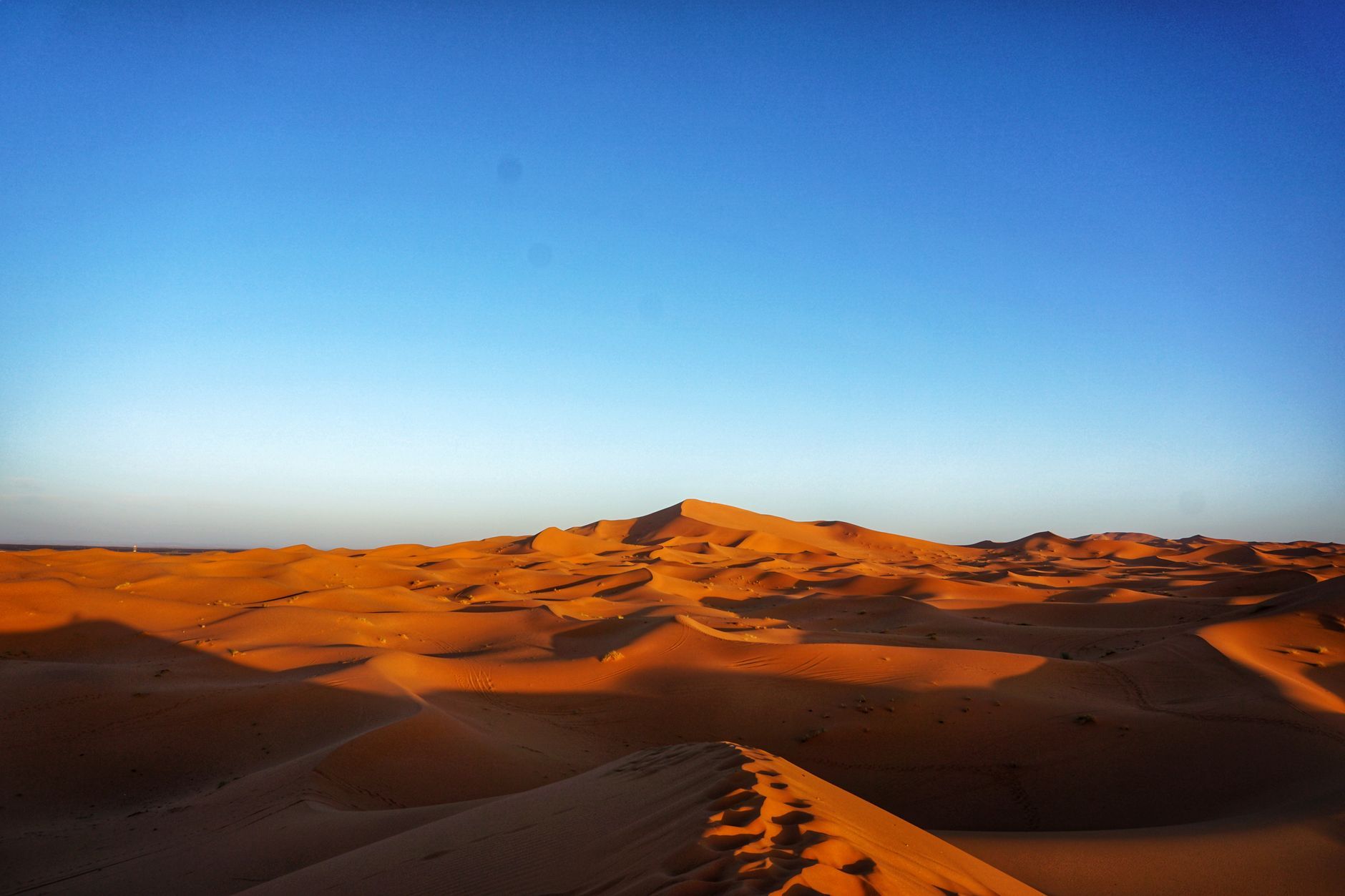 Capture the stunning beauty of expansive orange dunes beneath a vast blue sky, perfect for adventure or travel themes.