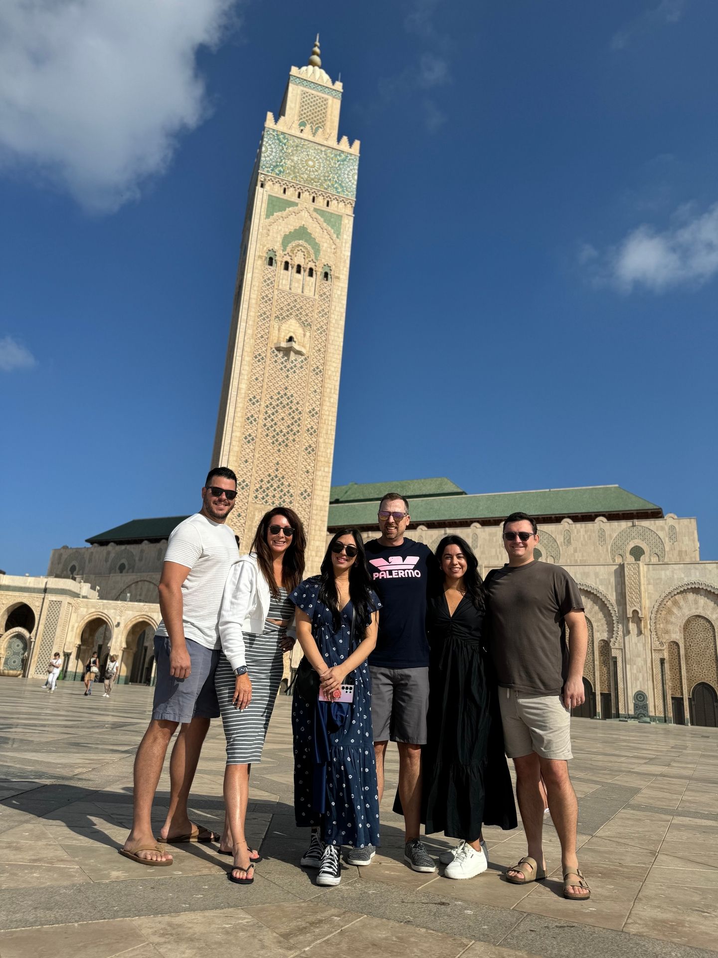 Six guests from an AZA Morocco Tours trip in front of the Hassan II Mosque minaret in Casablanca