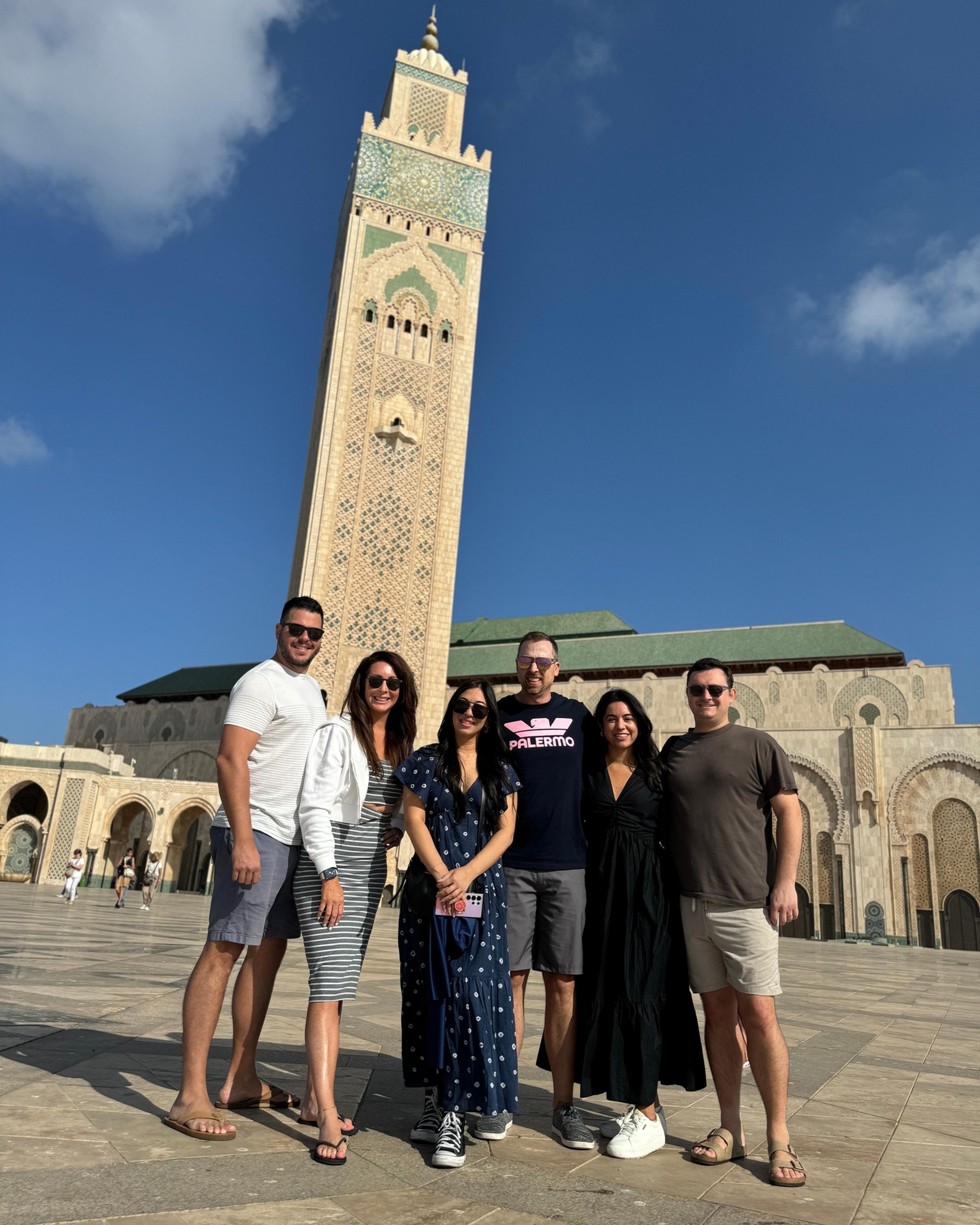 Six guests from an AZA Morocco Tours trip in front of the Hassan II Mosque minaret in Casablanca