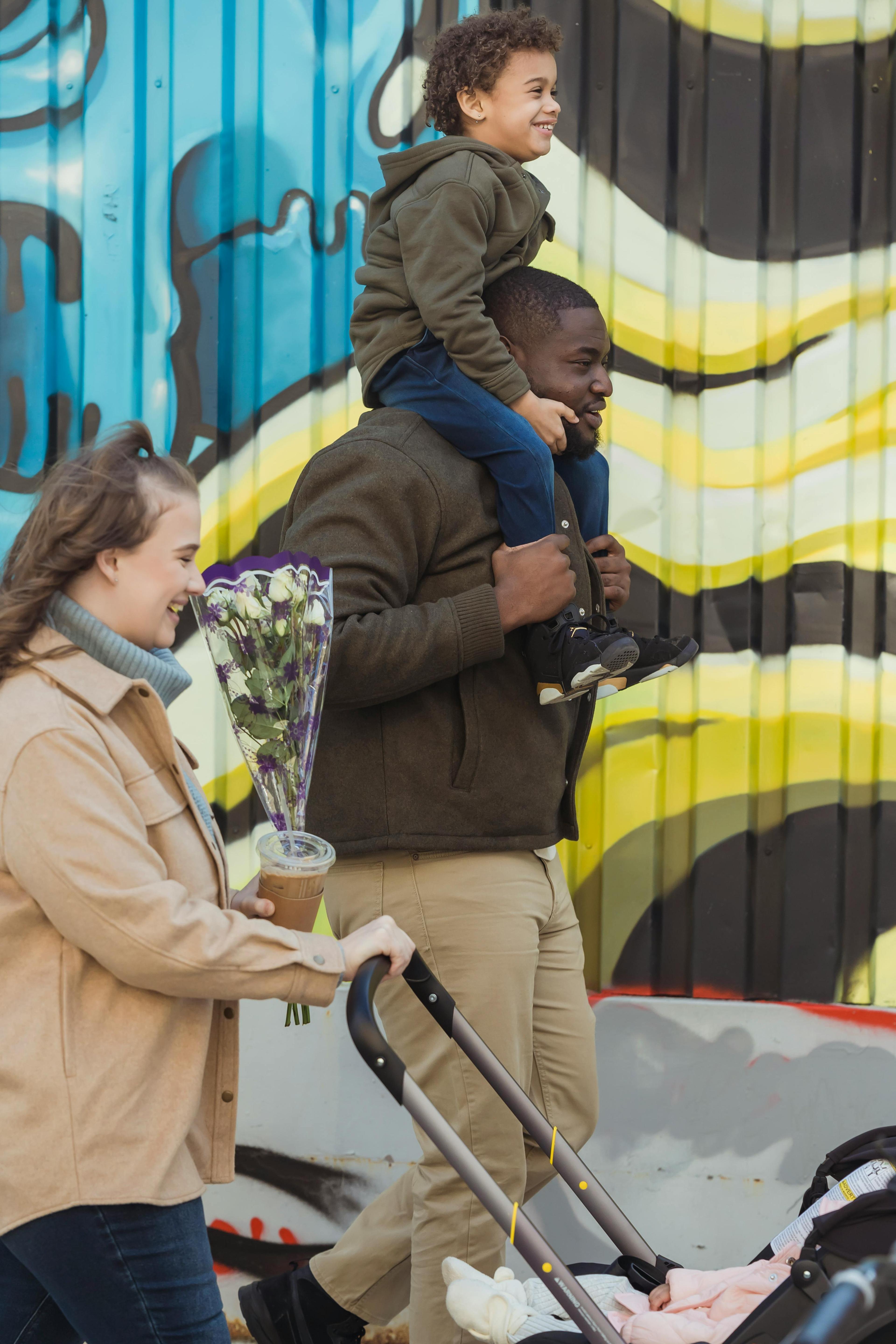 Man carrying his child and a woman pushing a child in a stroller, showcasing an equal relationship.