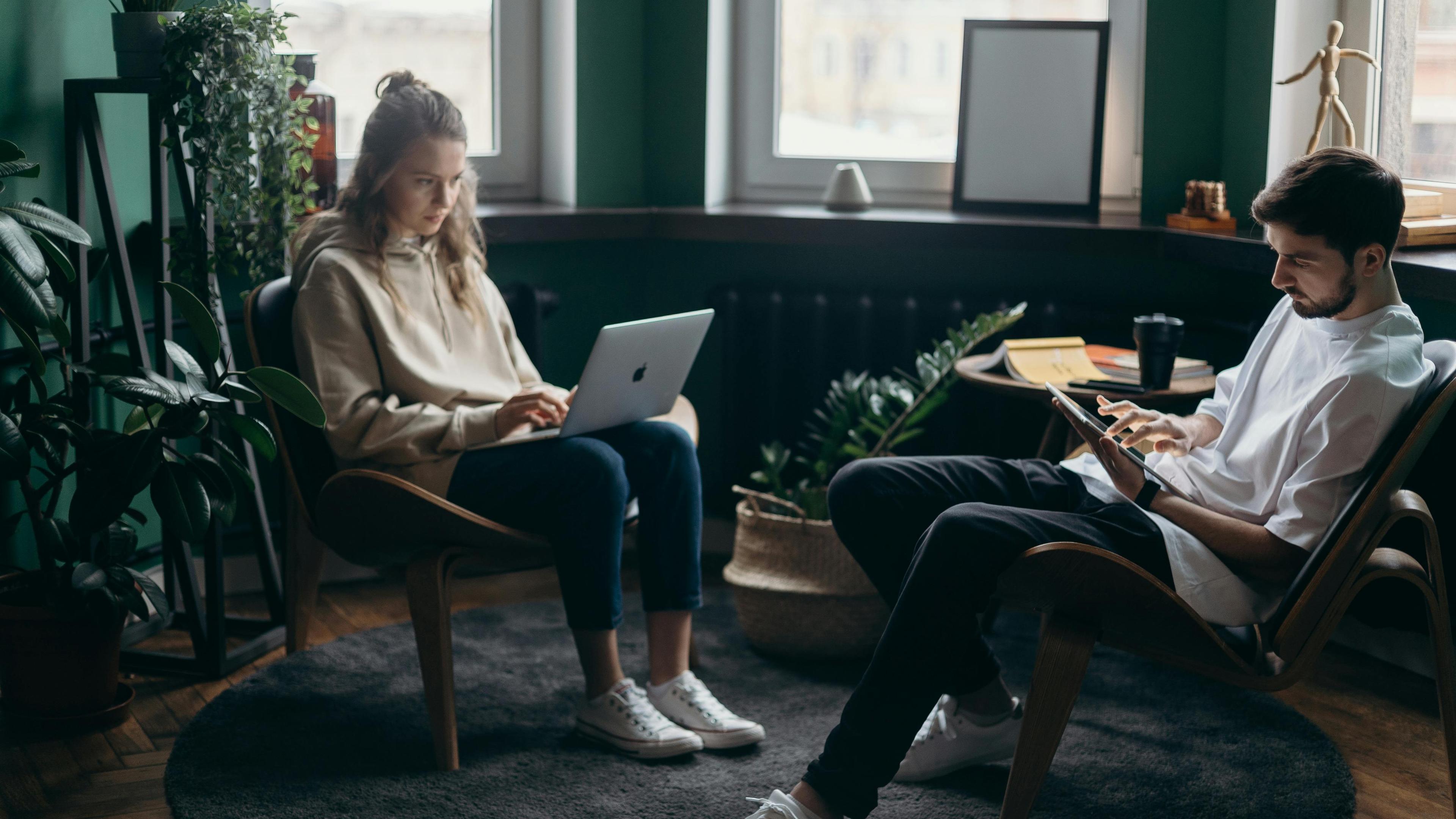 A couple sitting in a livingroom with eletronic devices and they're in a relationship without intimacy.