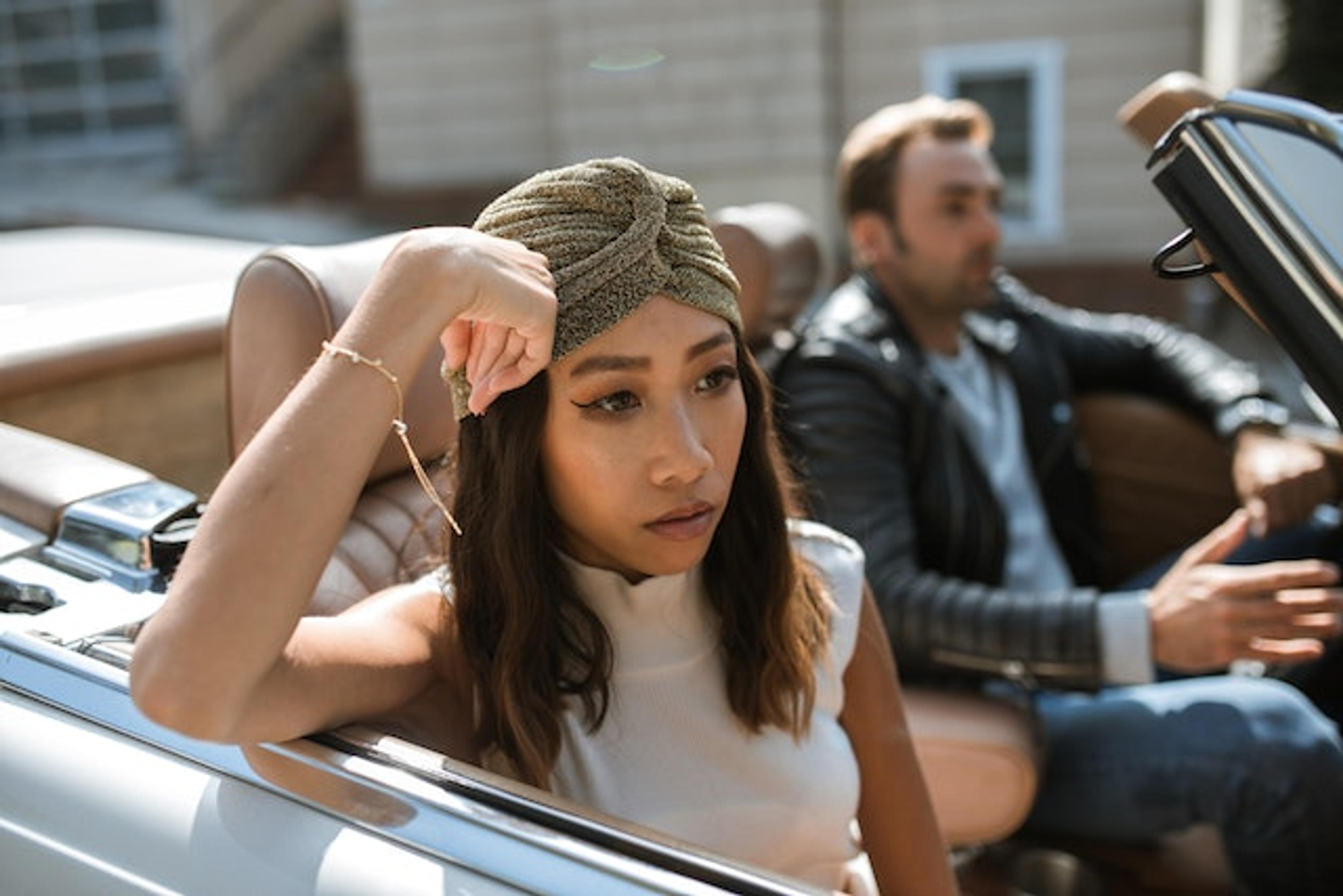 A woman sitting in a convertible car with a man in the back seat, symbolizing a misunderstanding in relationships.