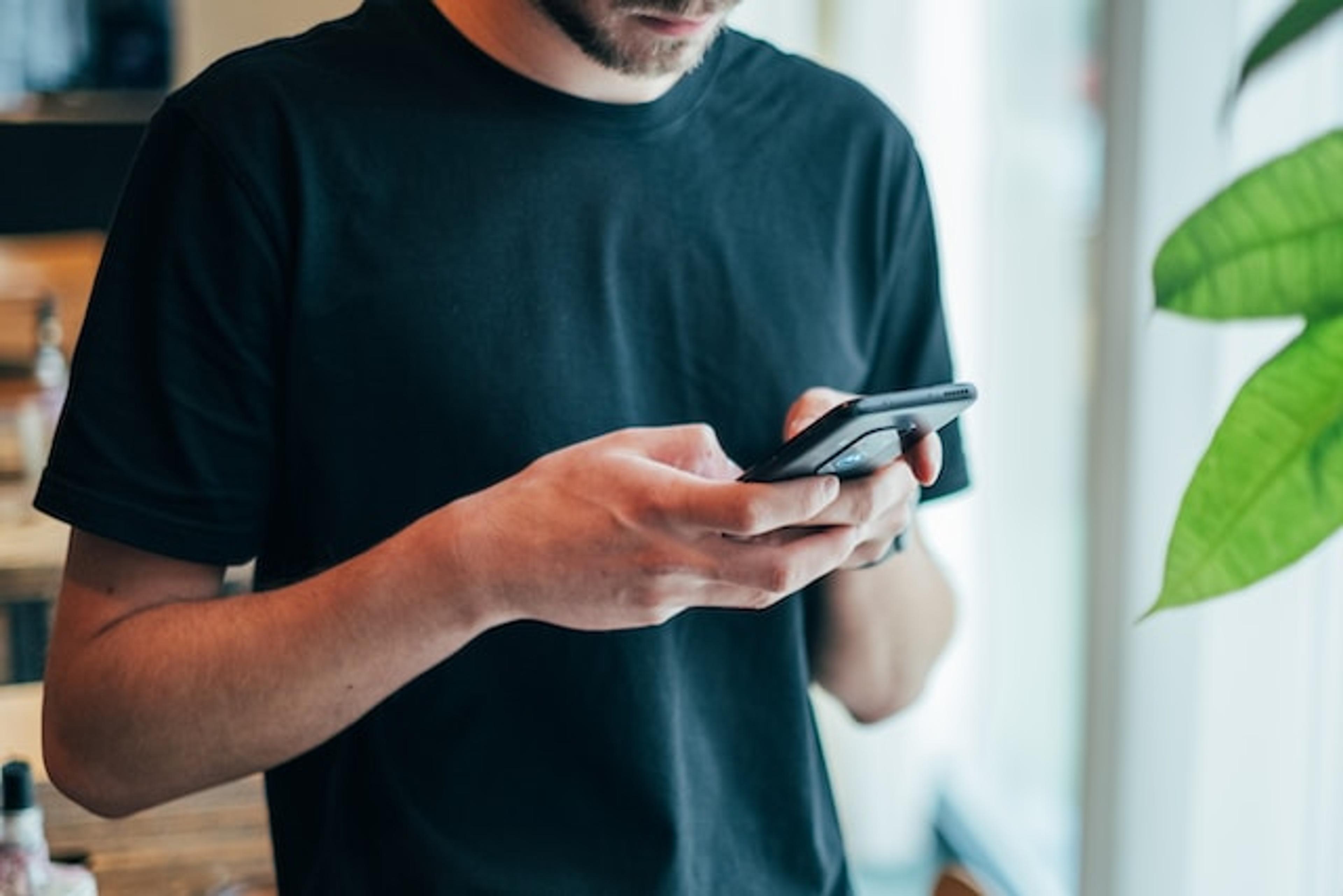 A man wearing a black shirt focused on his phone screen, is sexting cheating
