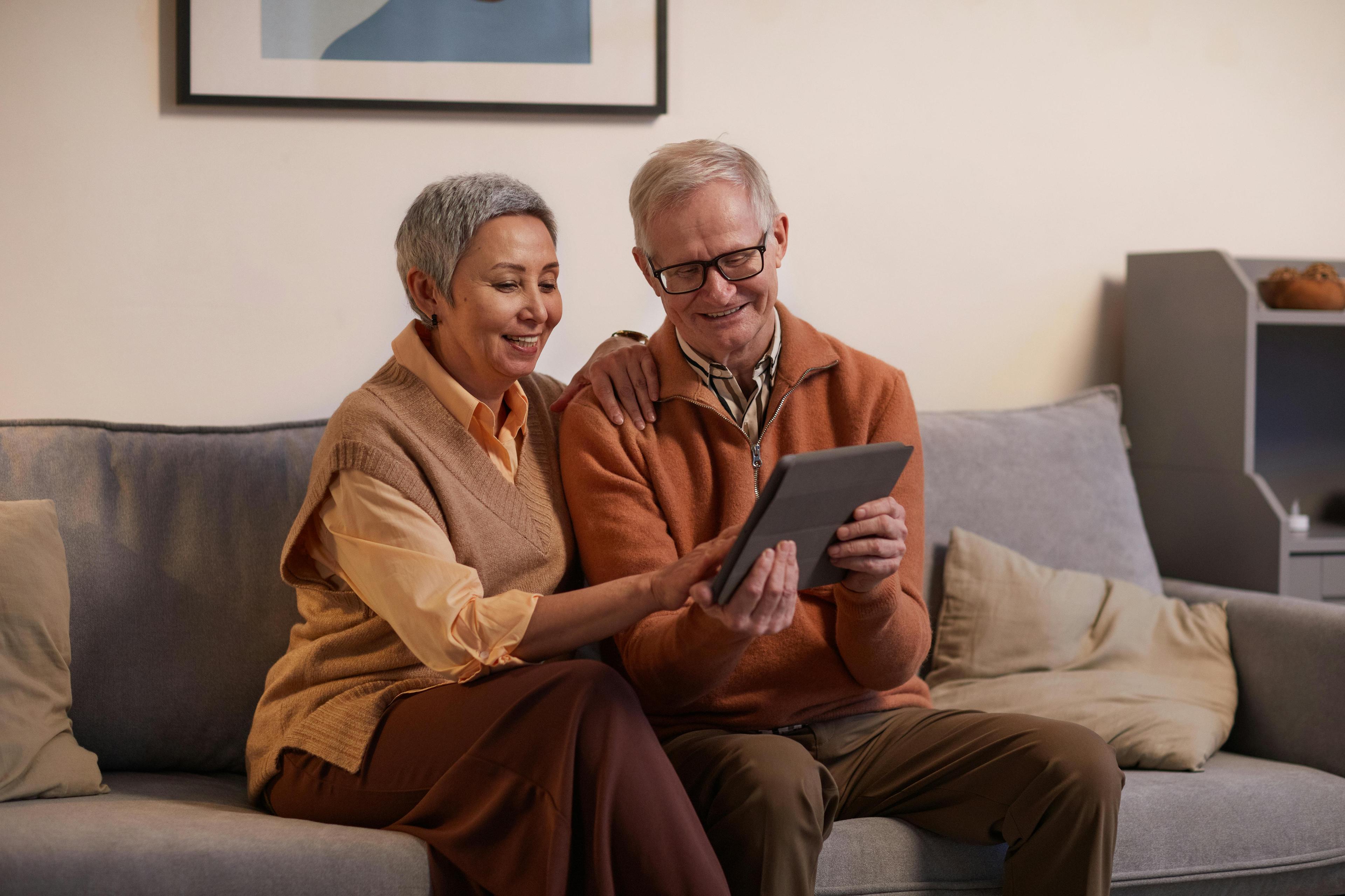  Senior couple sitting on sofa, using tablet for help with relationship.