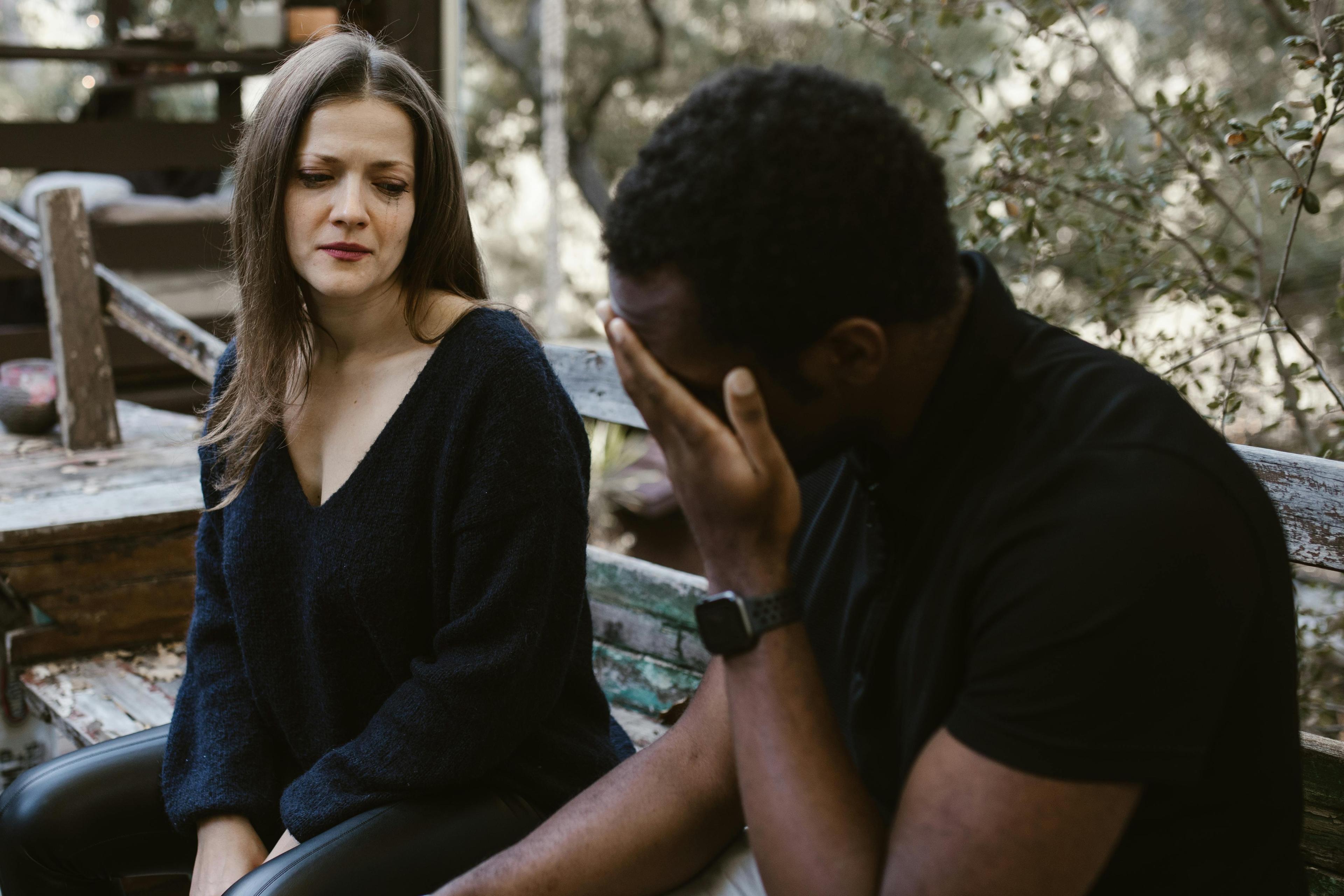 A woman and a man sitting on a bench, looking distant and disconnected, hinting at emotional cheating.