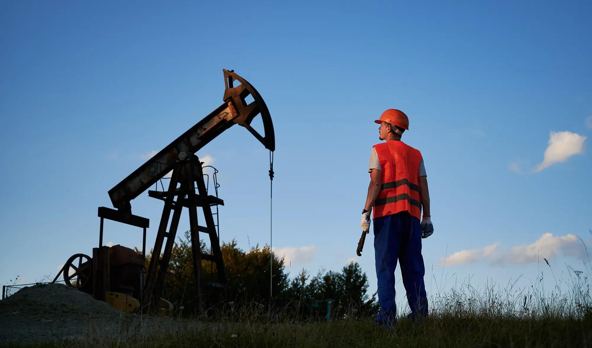 Oil field worker observing a pumpjack, representing renewed oil industry investment and production activity.