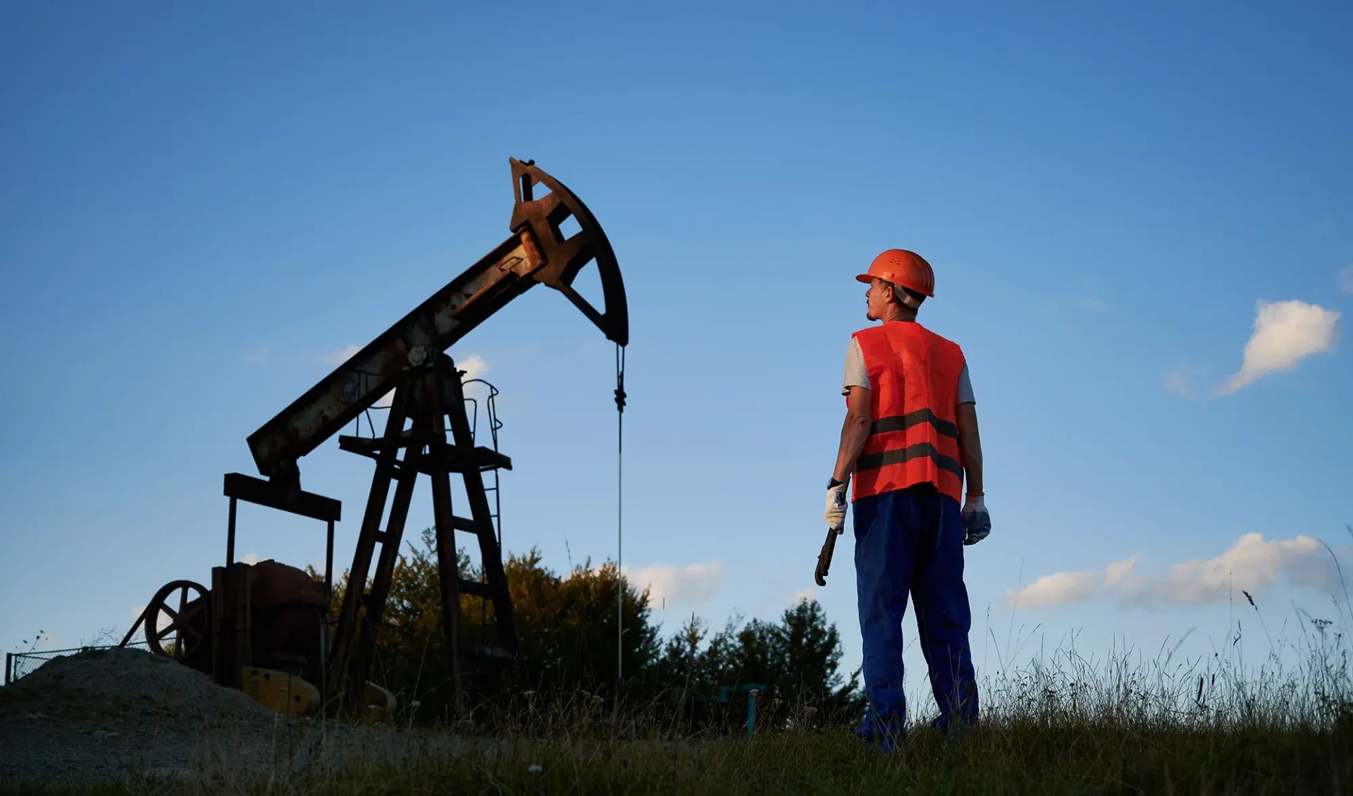 Oil field worker observing a pumpjack, representing renewed oil industry investment and production activity.