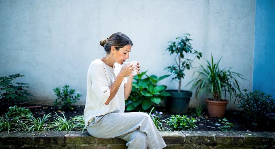 Una donna seduta su un muretto al sole, con una tazza in mano.