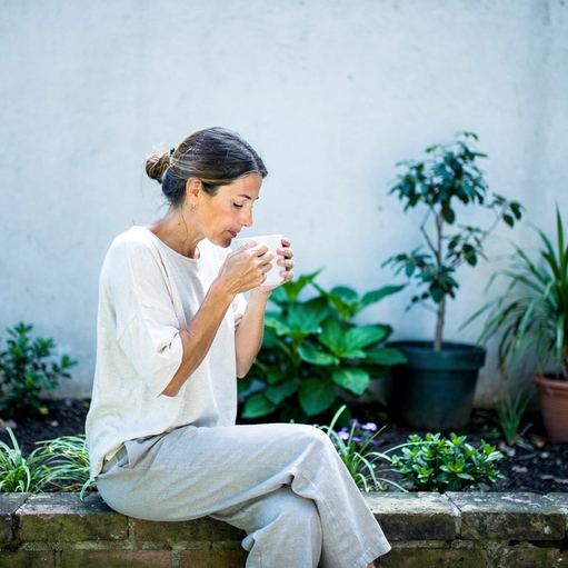 Una donna seduta su un muretto al sole, con una tazza in mano.