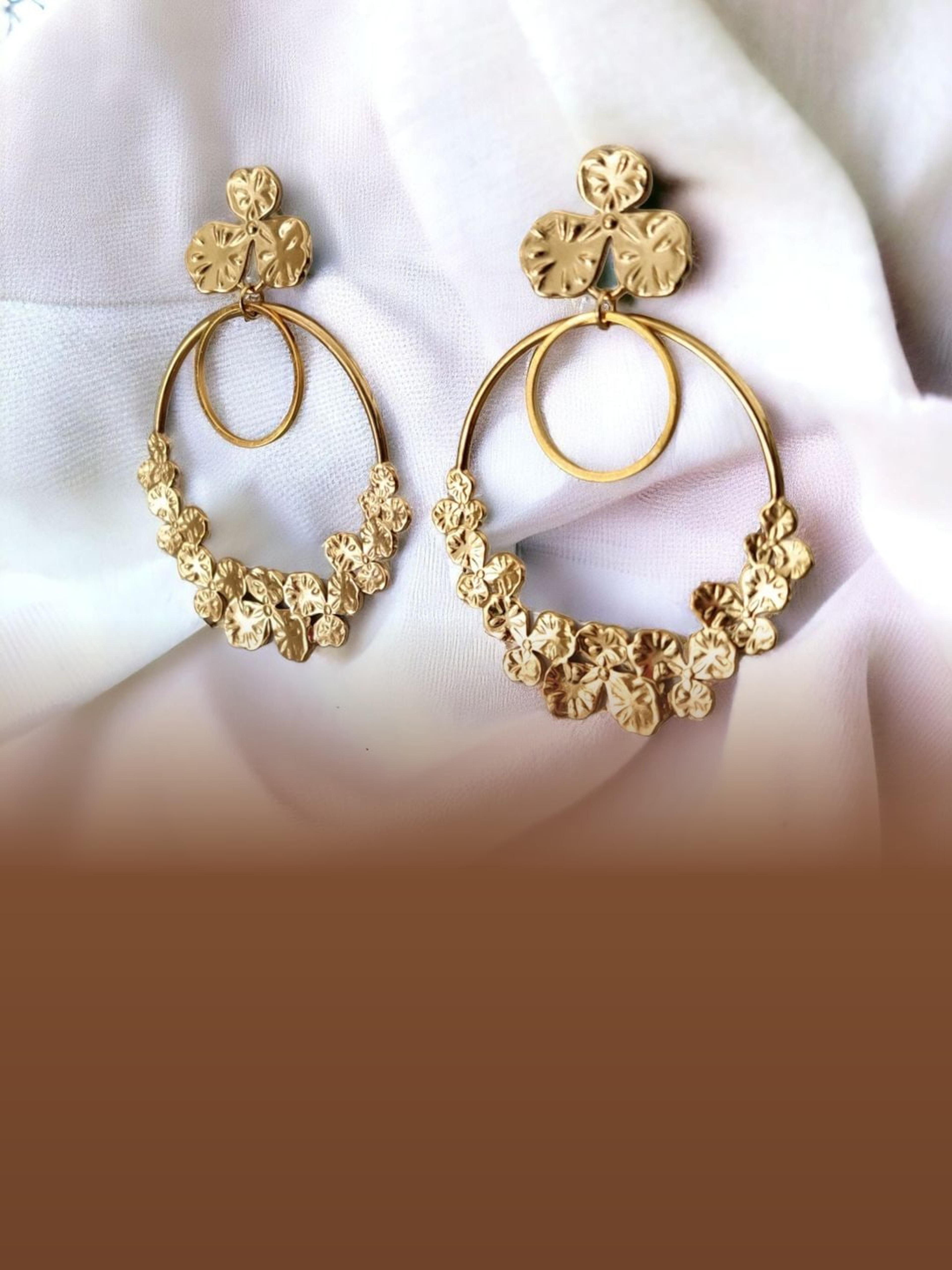 Boucles d'oreilles dorées à fleurs martelées posées sur un drapé blanc