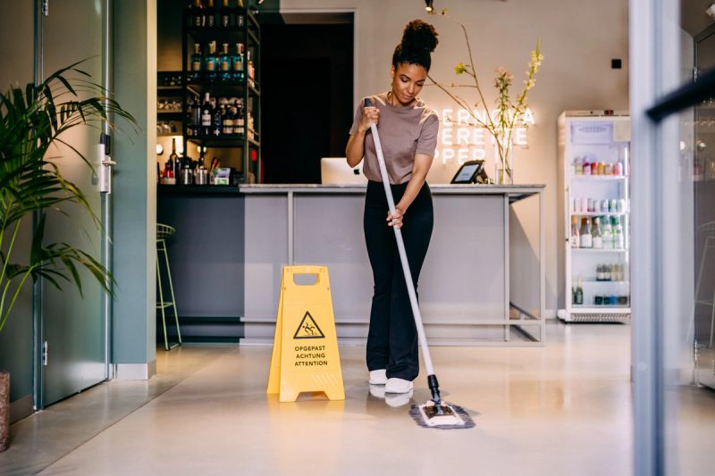 A woman mops a lobby floor next to a wet floor sign.