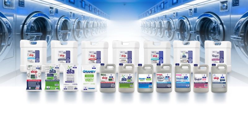 Assortment of laundry detergents and fabric softeners with industrial washing machines in the background.