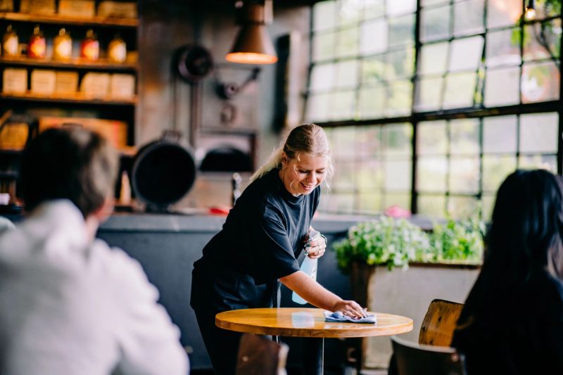 A smiling woman wipes a table in a cafe or restaurant.