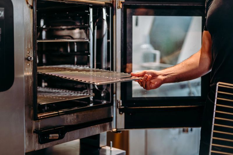 A hand placing a metal rack into an open commercial oven.