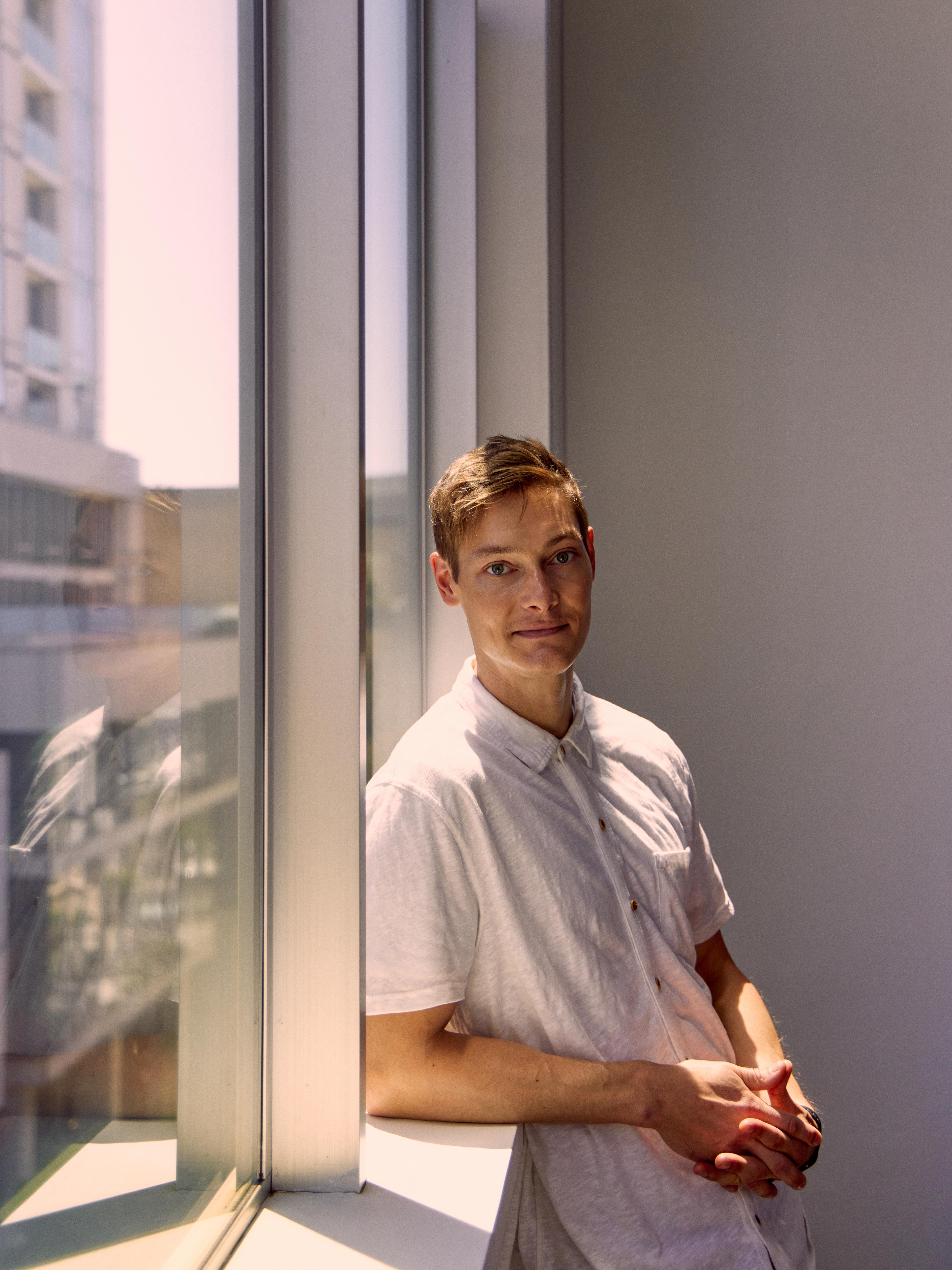 Photograph of Ryan Hoover leaning against the window of his home | Derek Yarra for Meridian