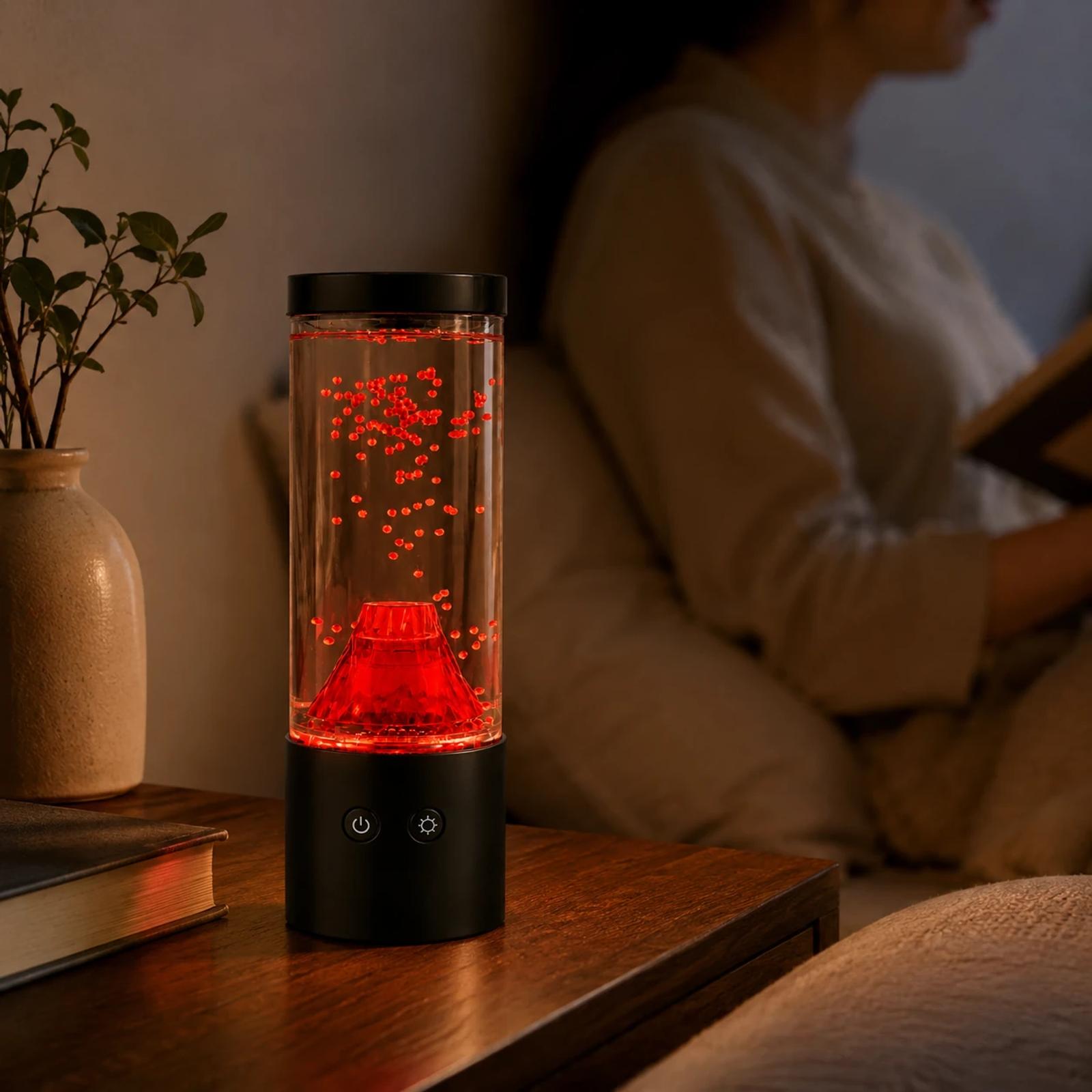 MX-5015V volcano night light glowing on a bedside or desk surface with a blurred person in a warm bedroom decor scene.