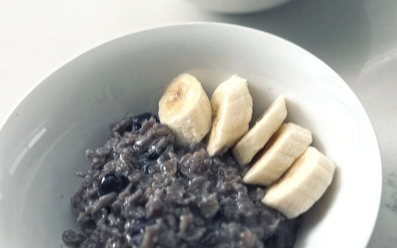 A bowl of purple blueberry oatmeal topped with banana slices