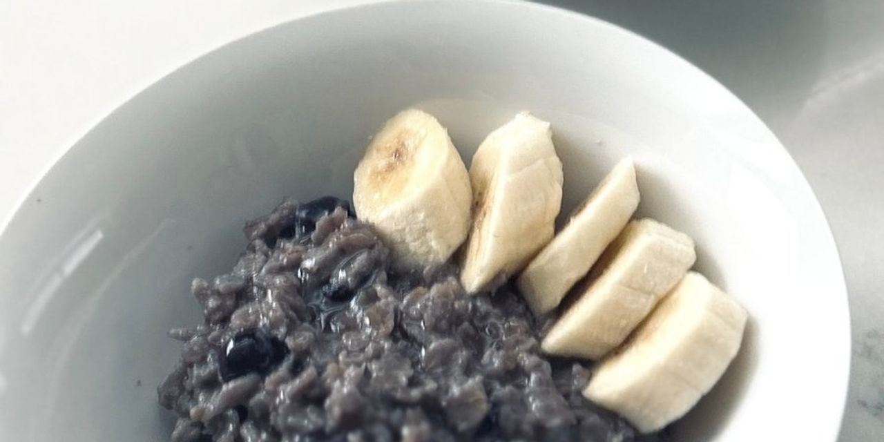 A bowl of purple blueberry oatmeal topped with banana slices