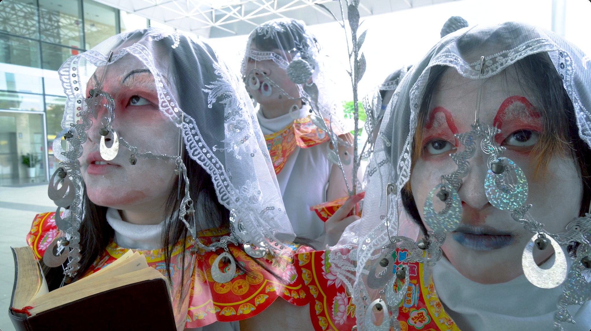 Three figures wearing white veils and silver jewellery.