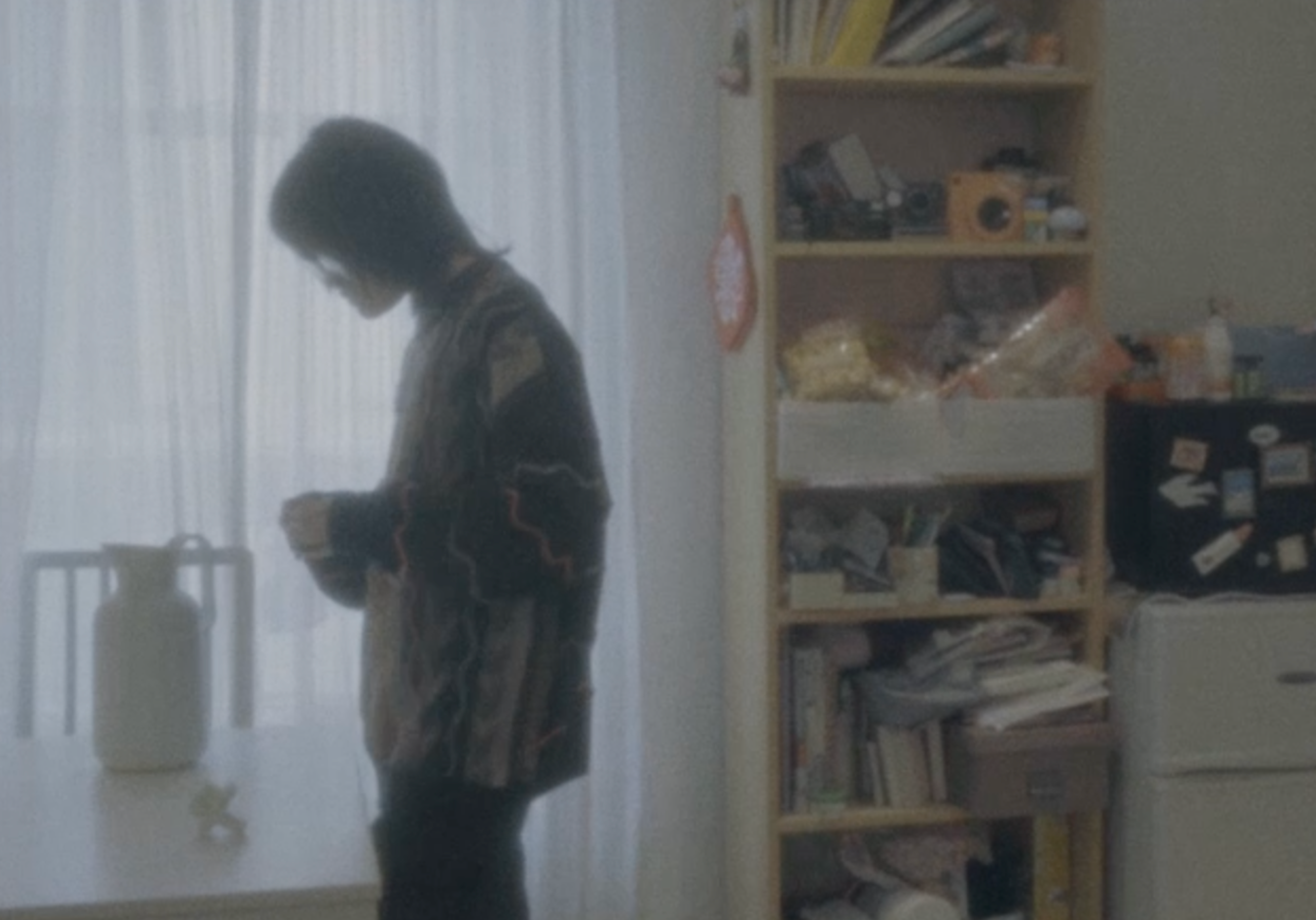 A person wearing glasses and a stripy jumper next to a bookcase.
