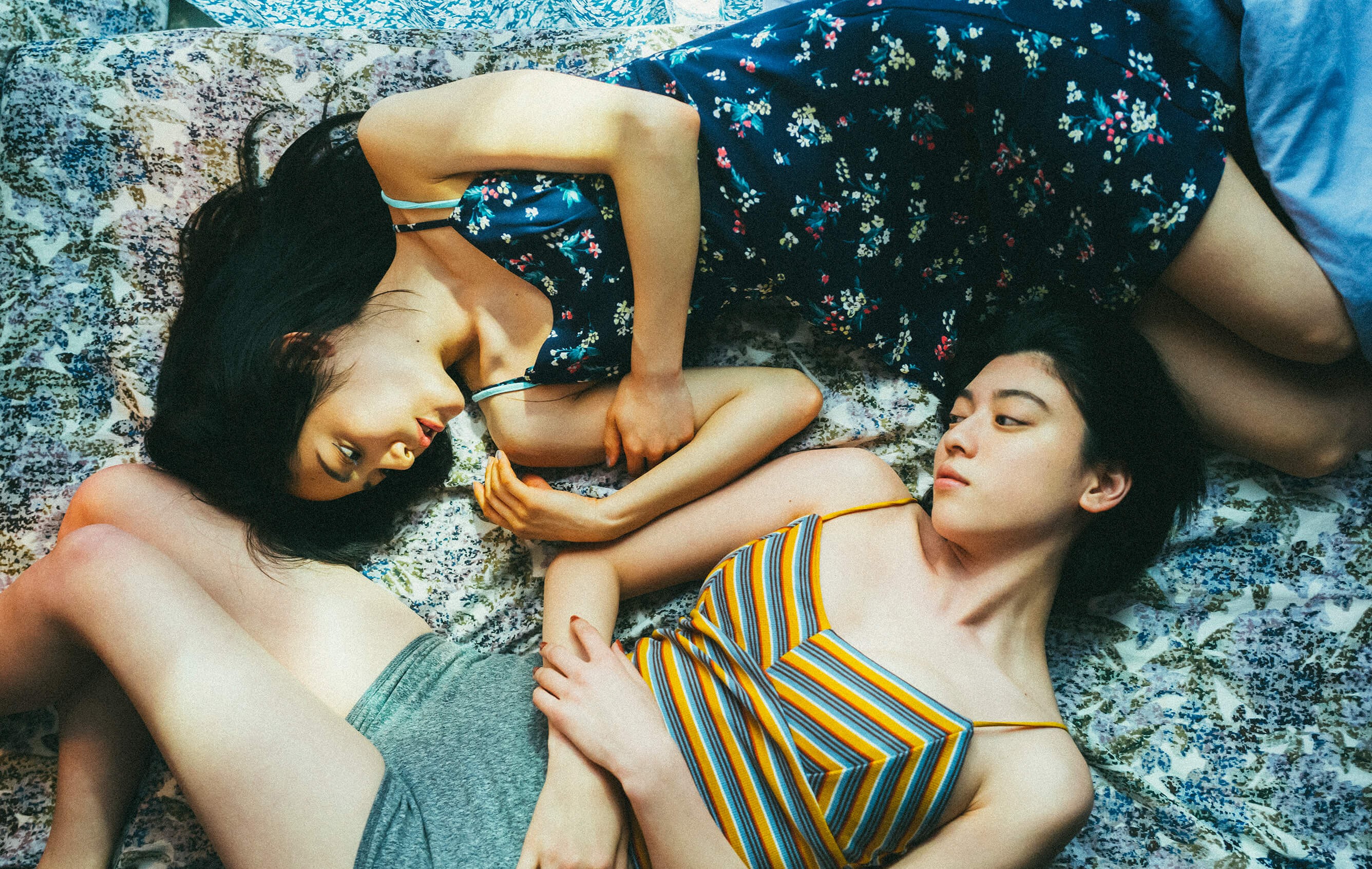 Two women lying on the ground with their arms touching.