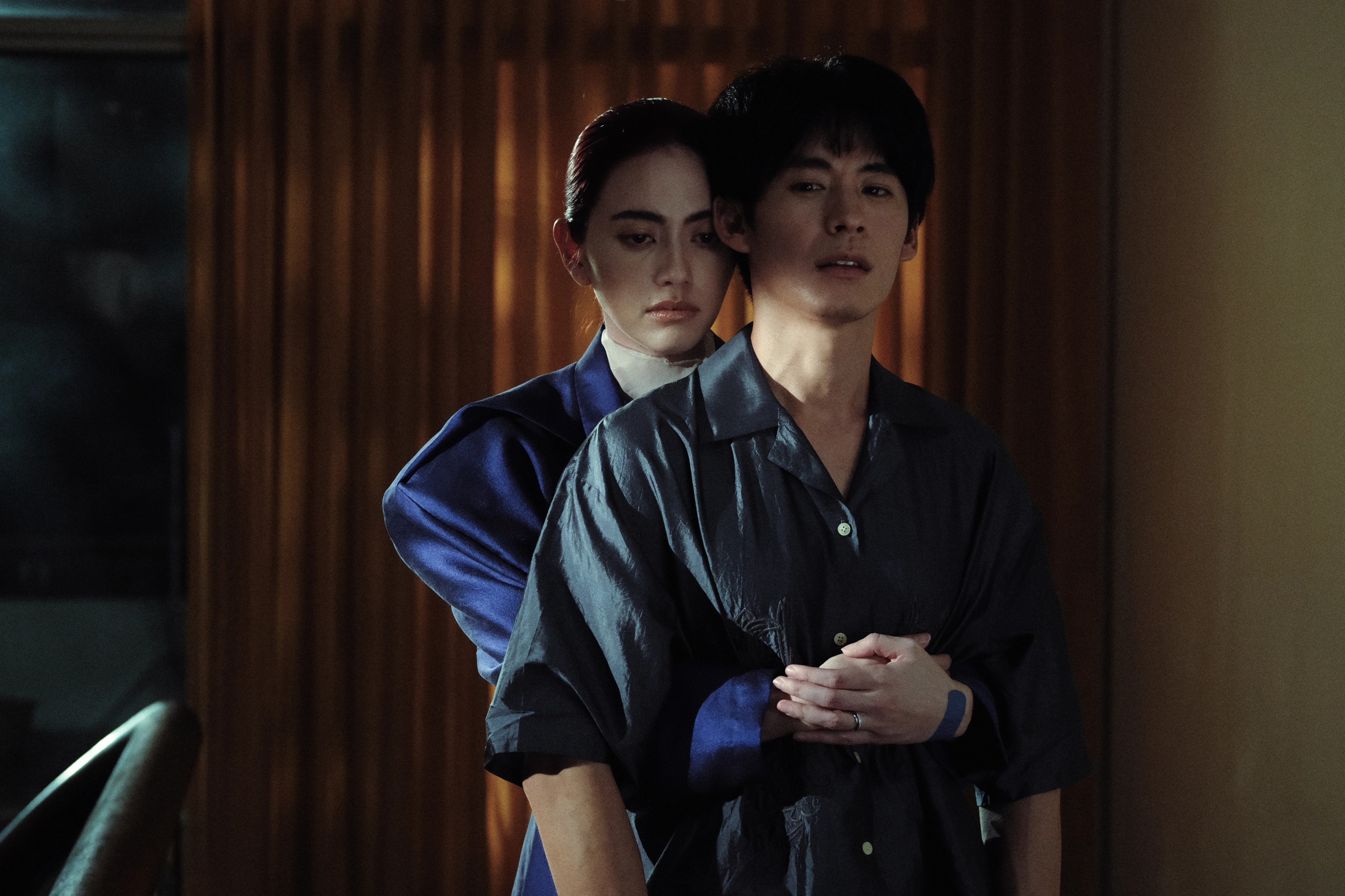 A person standing behind another person and holding them around the waist indoors.