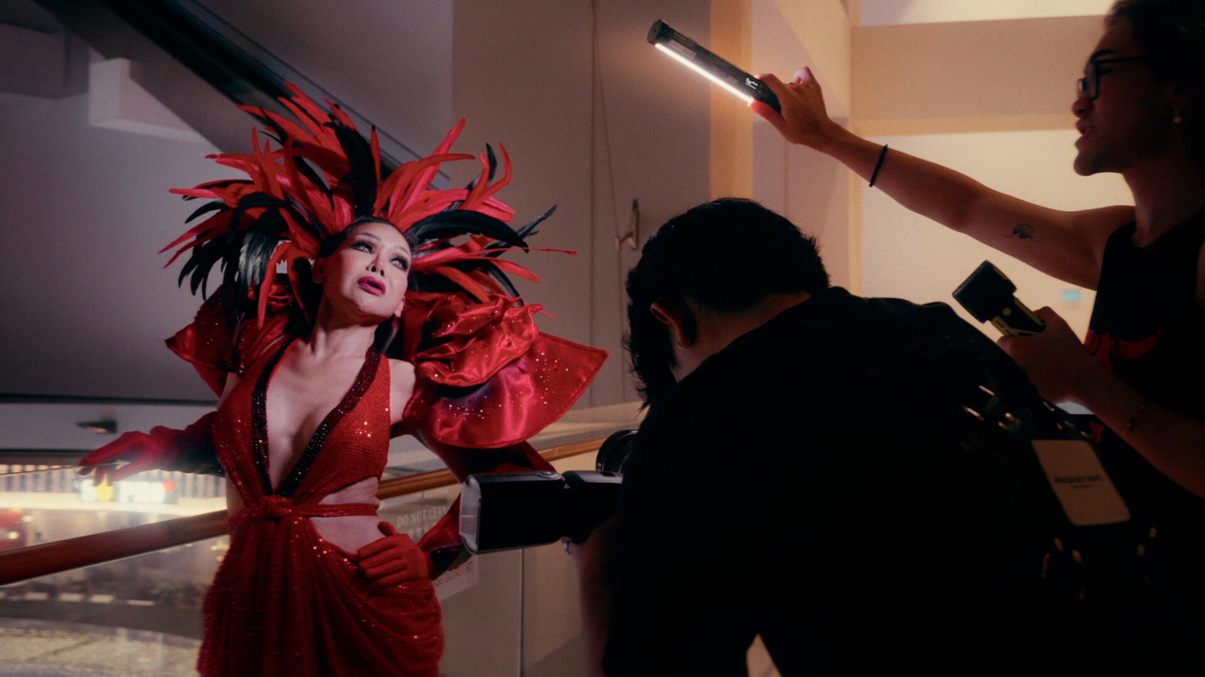 a woman in a red dress and headpiece is photographed by a camera crew.