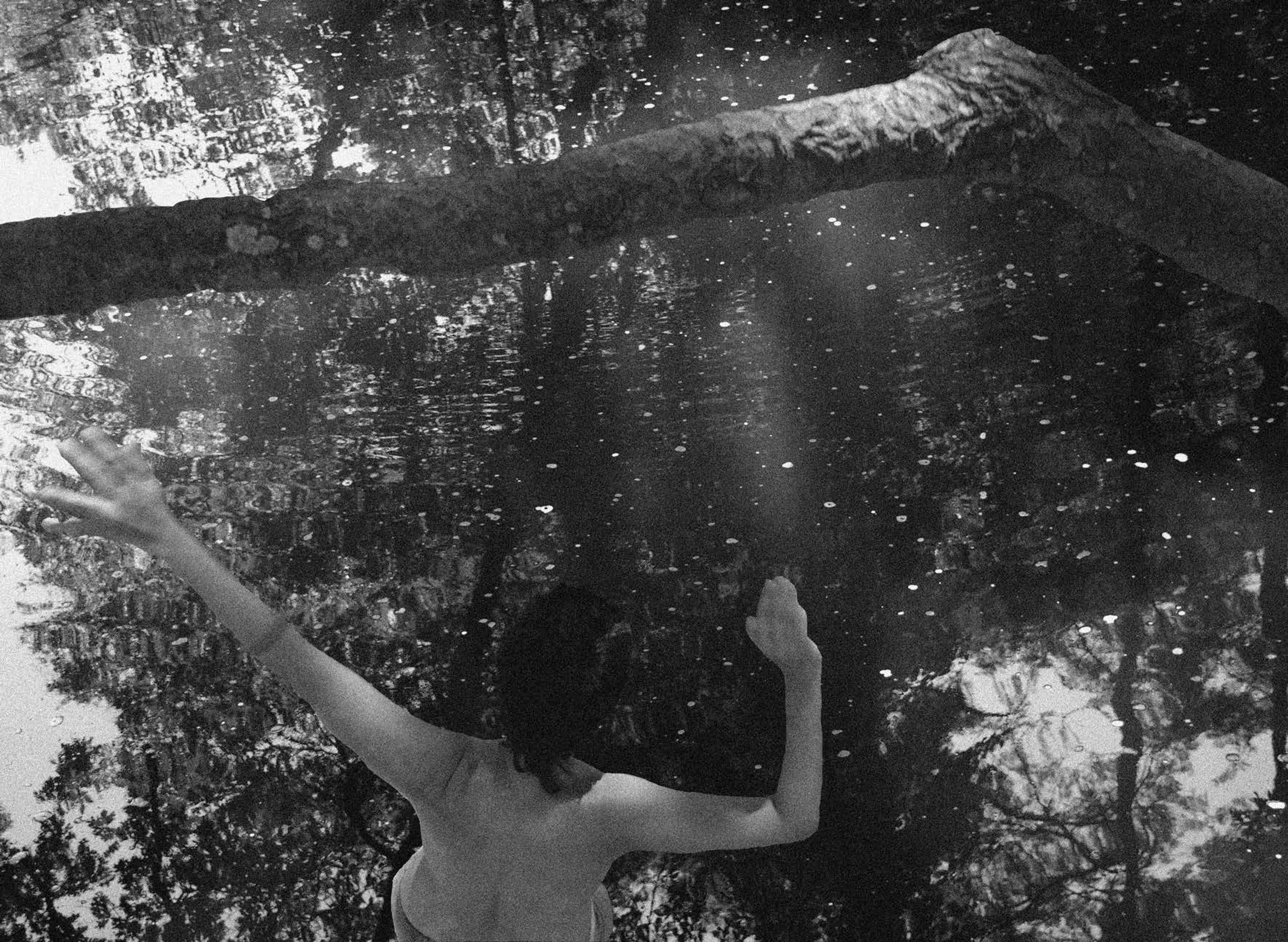 A person with outstretched arms by a body of water.