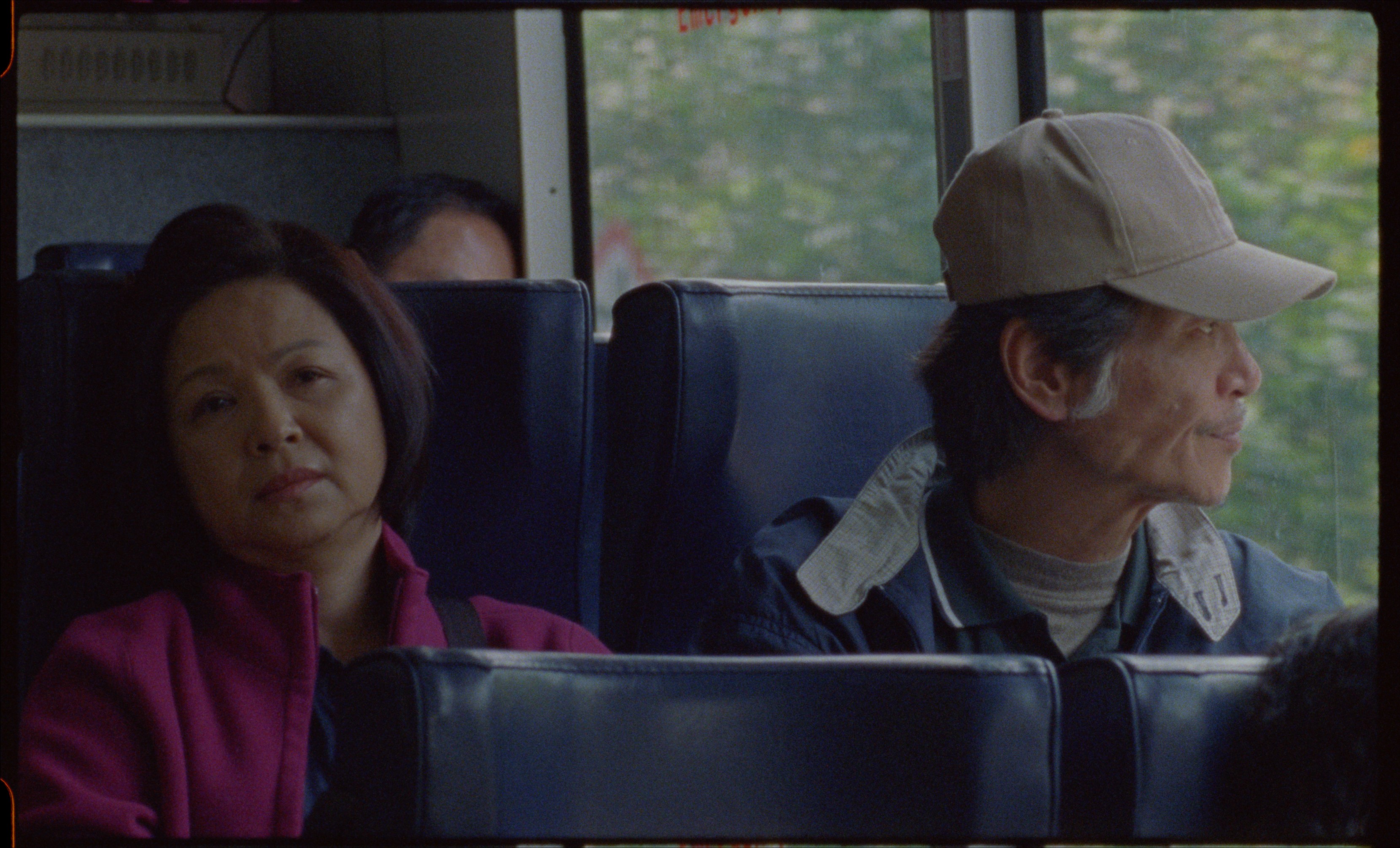 A woman and man seated beside each other on a bus, with the man looking out the window.