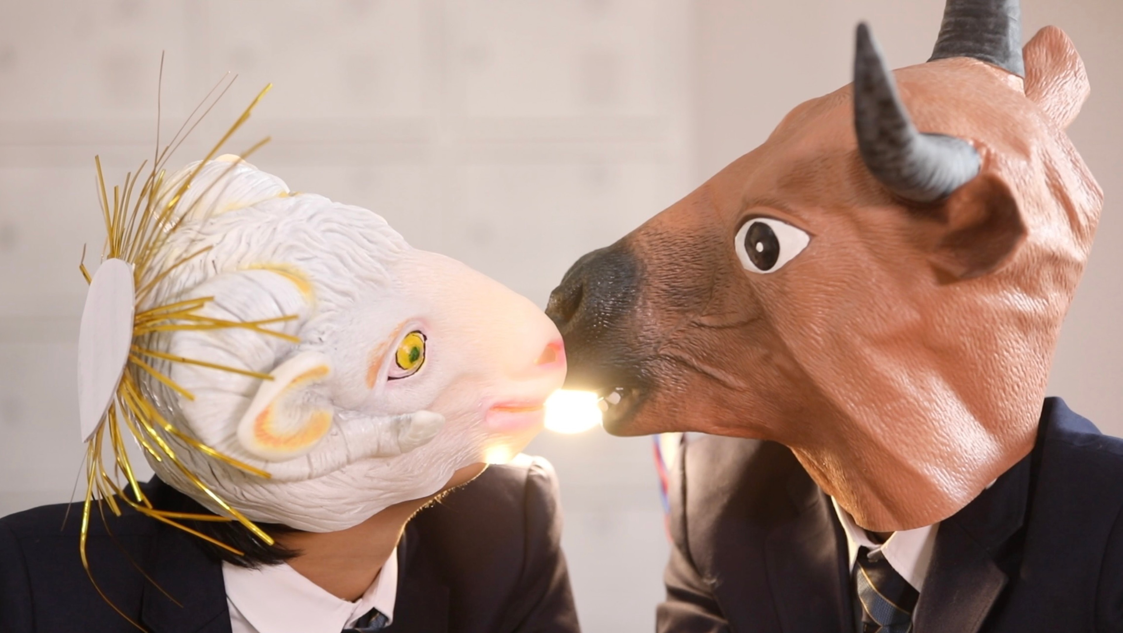 A person wearing a lamb mask kisses a person wearing a bull mask.