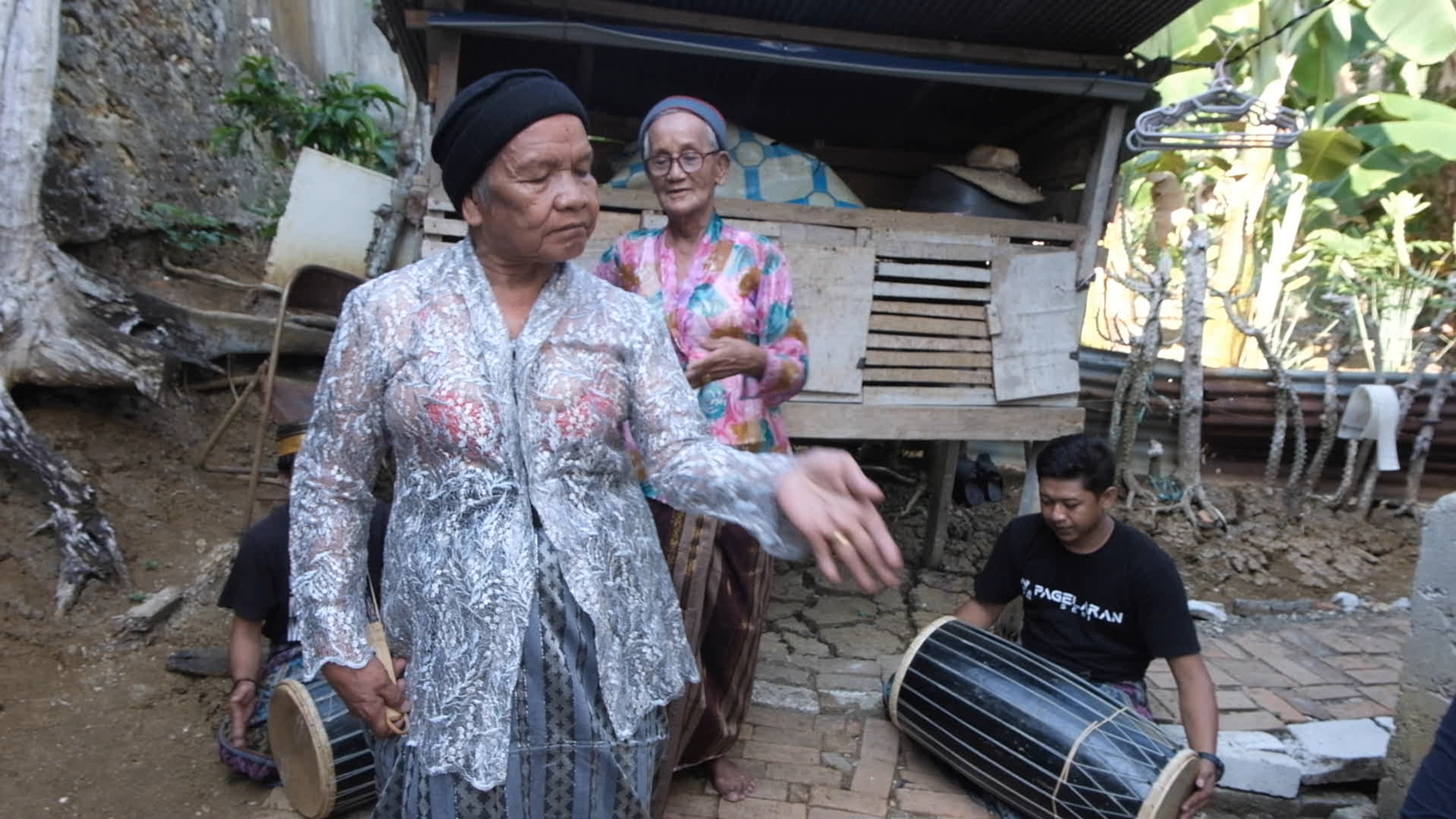 An older woman dancing outdoors while musicians play drums behind her.