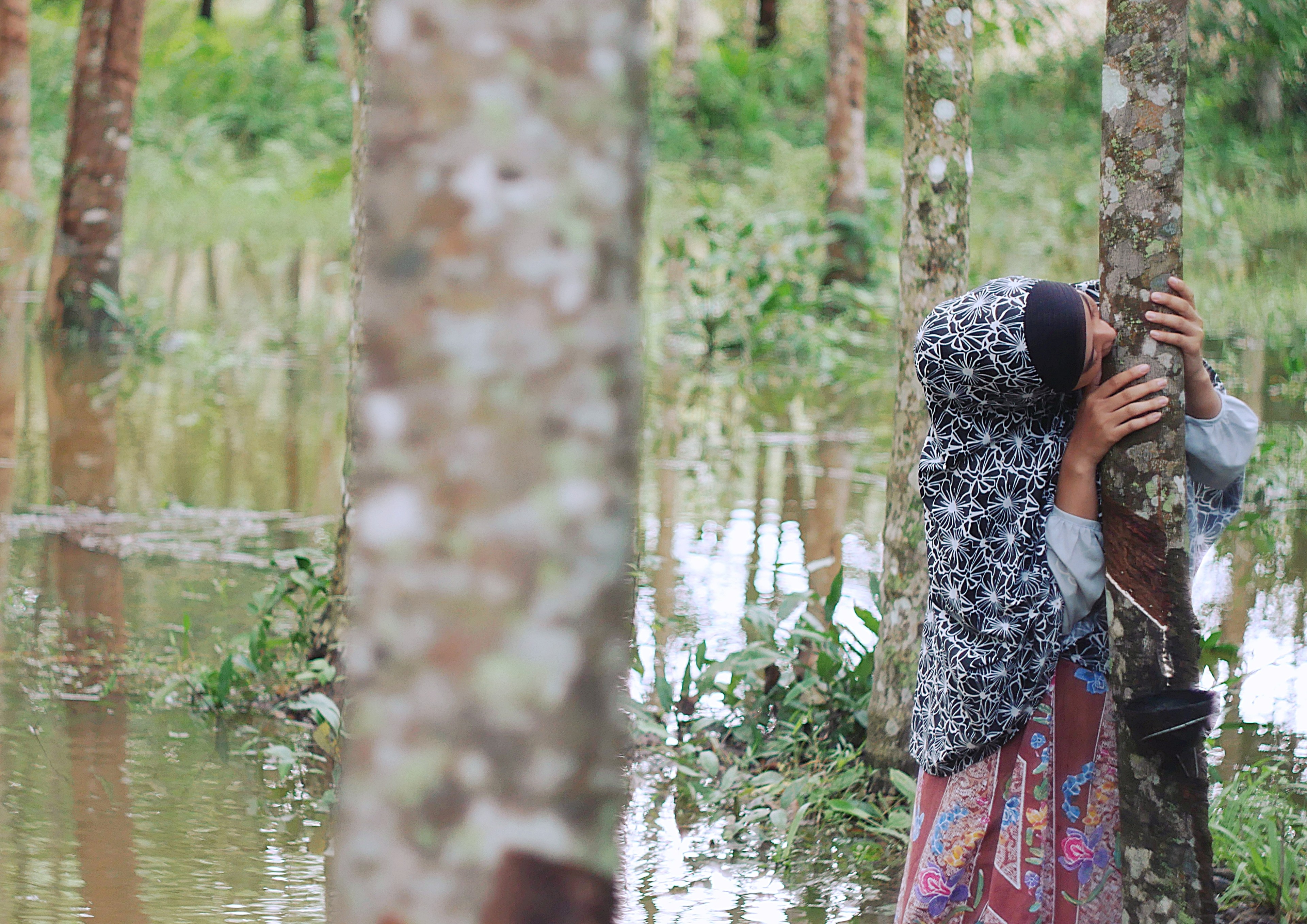 A woman in a patterned headscarf embracing a tree in a flooded forest.