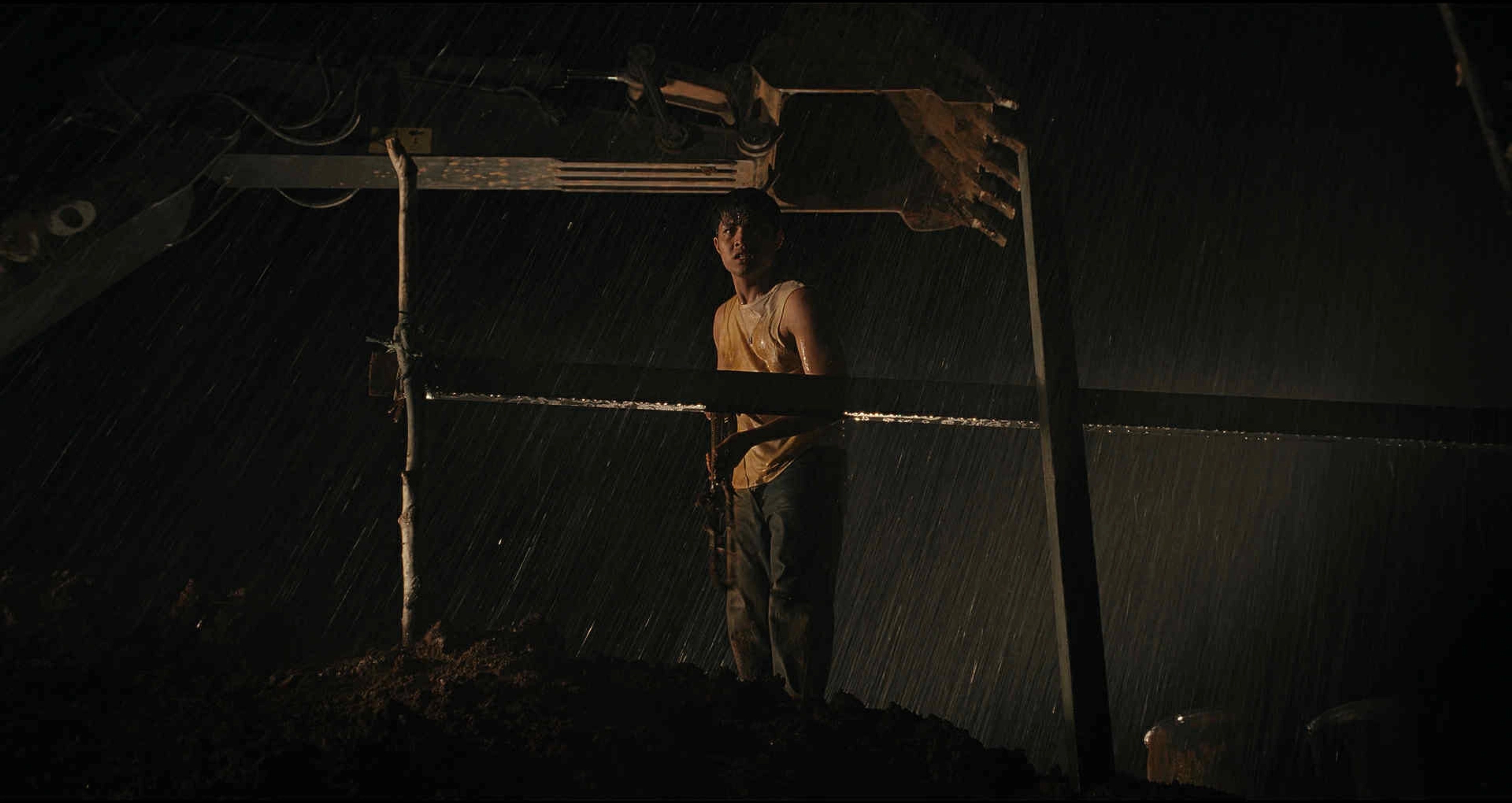 A man standing alone in heavy rain at night beneath a dark metal structure.
