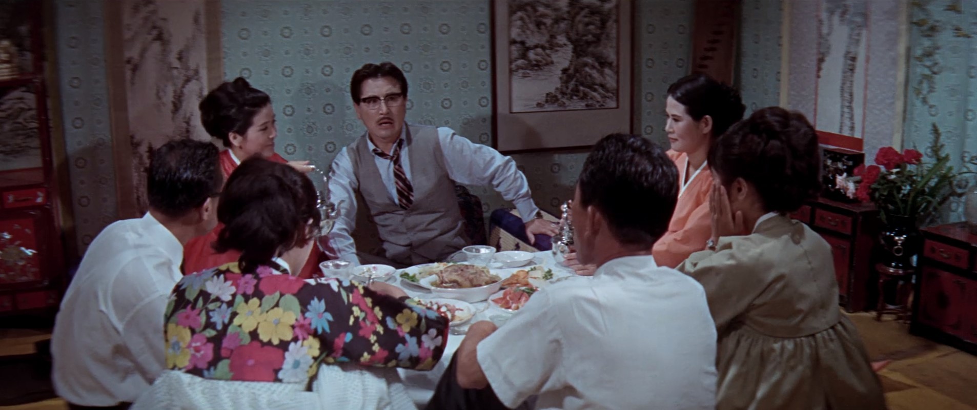 A group of people gathered around a dining table during a meal, with one man speaking at the centre.