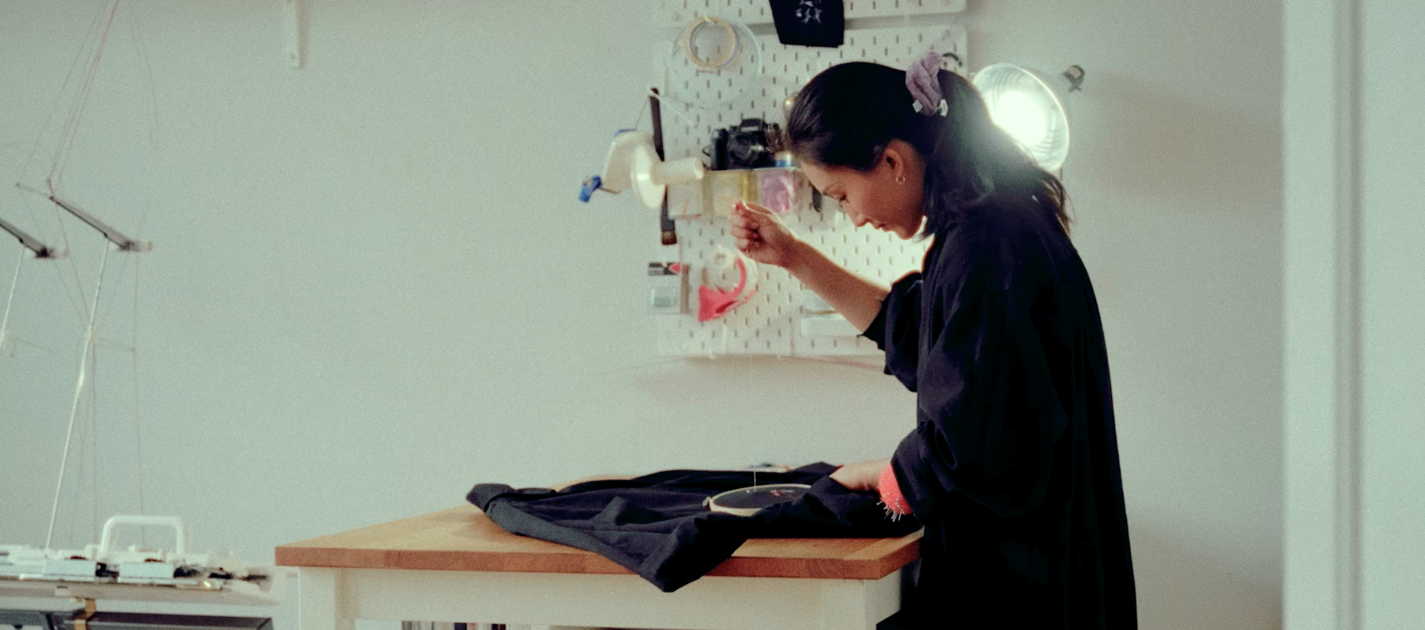 A woman working on a garment at a table in a sewing studio.