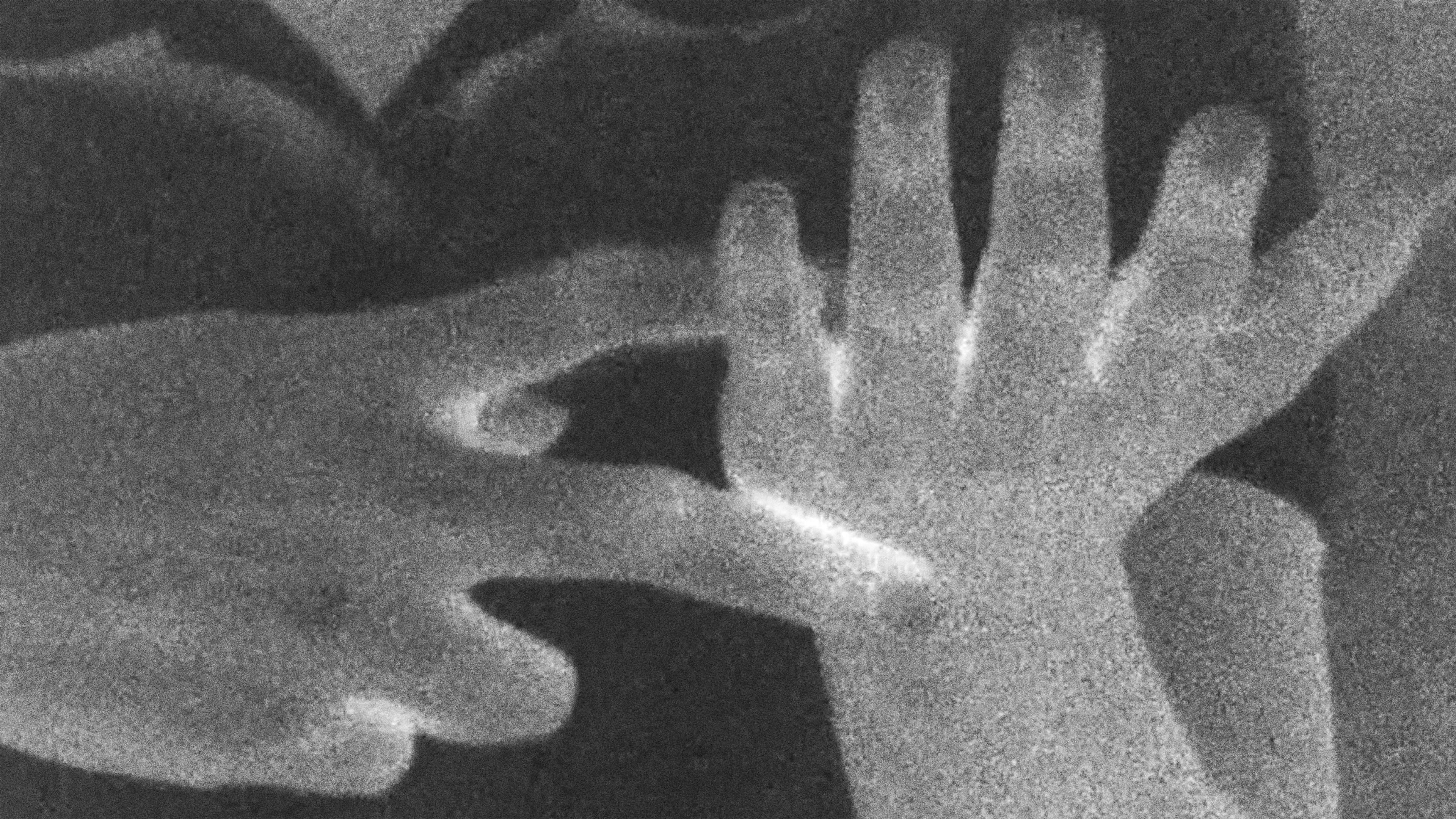 A grainy black-and-white image of two overlapping hands, one reaching toward the open palm of the other.