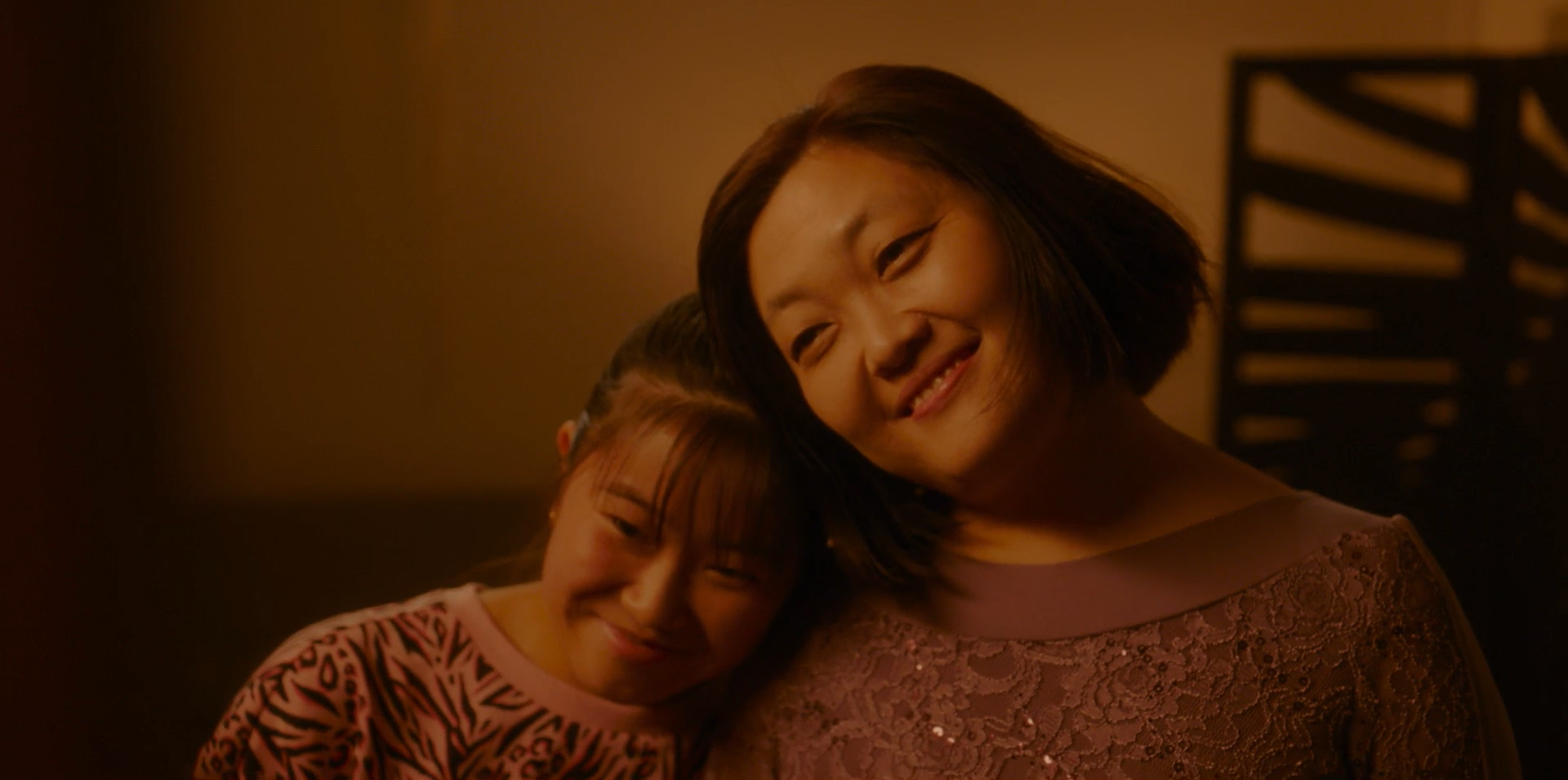 Two women smiling as one rests her head affectionately on the other’s shoulder.