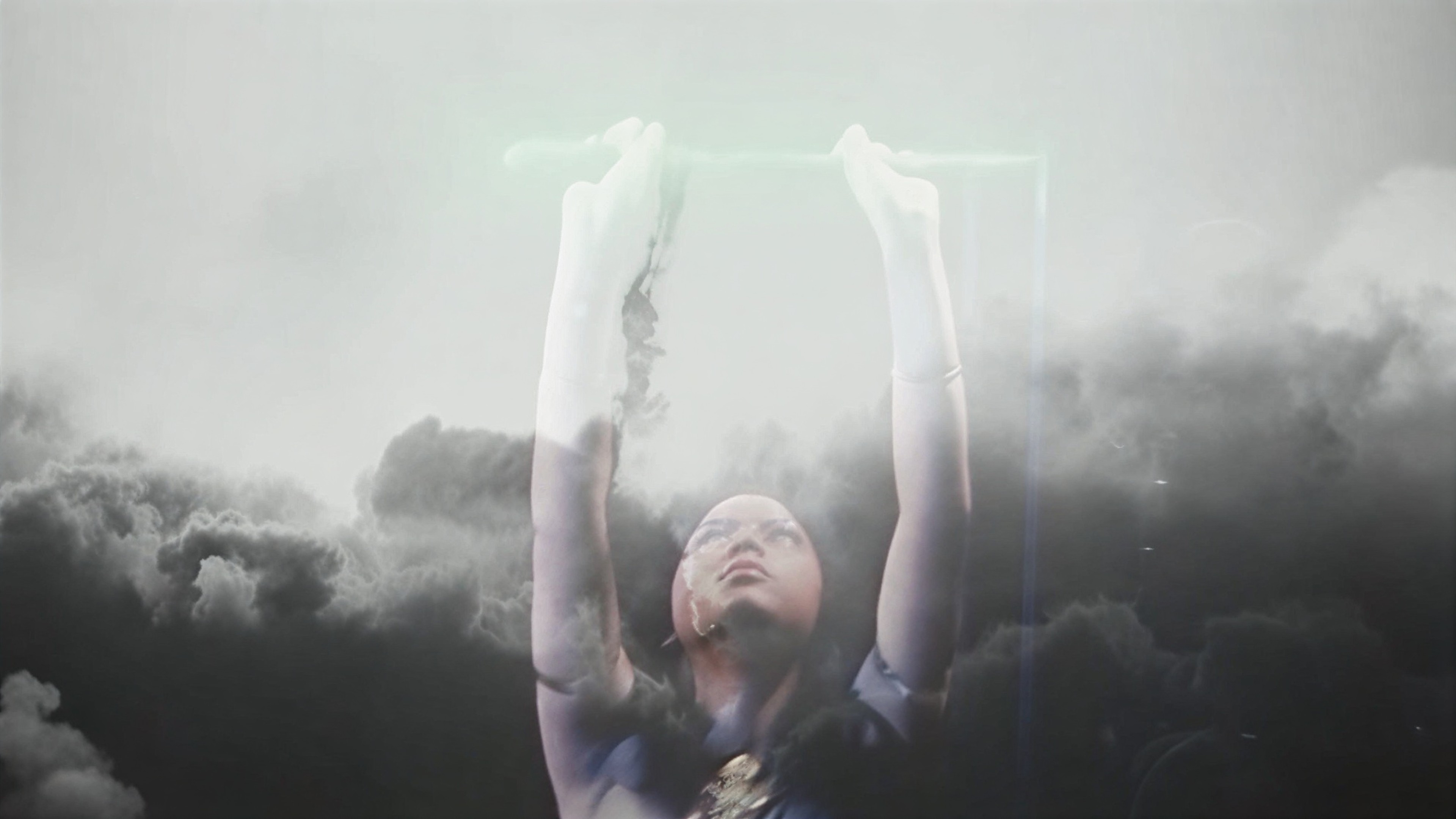 A person raising both arms overhead against a dramatic backdrop of dark clouds and bright light.