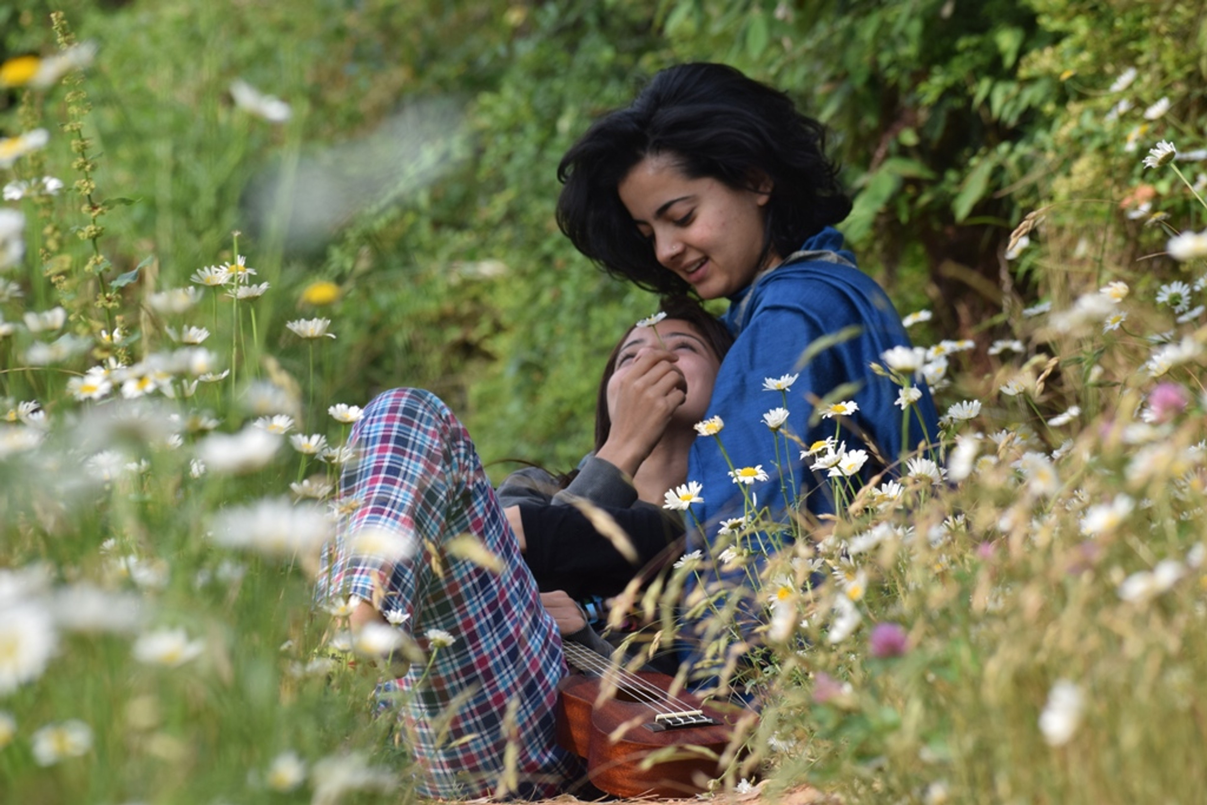 A girl lies in the lap of another girl amid a bed of flowers.
