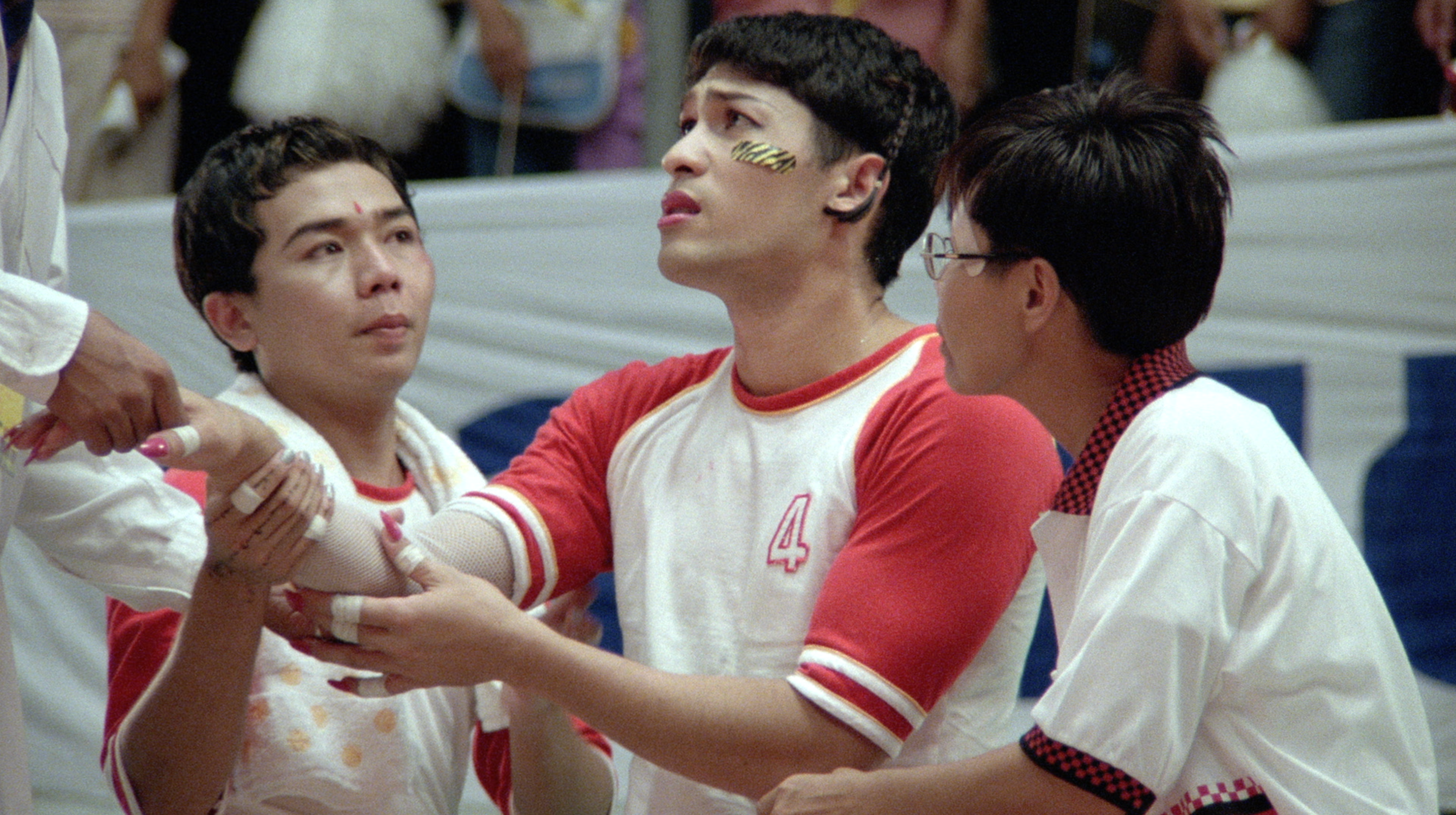 Three young men in sports uniforms gathered closely around an injured teammate during a game.