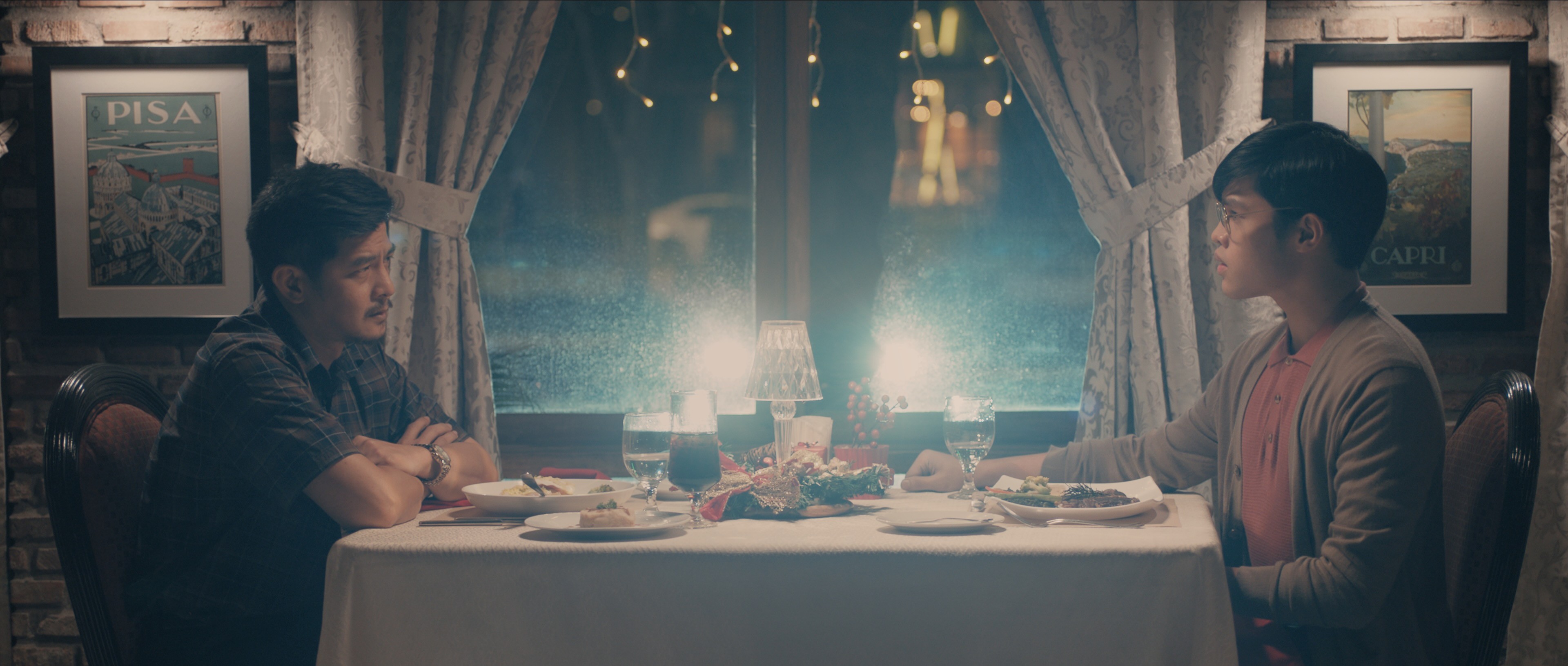 Two men seated across from each other at a restaurant table, facing one another over dinner in a softly lit interior.