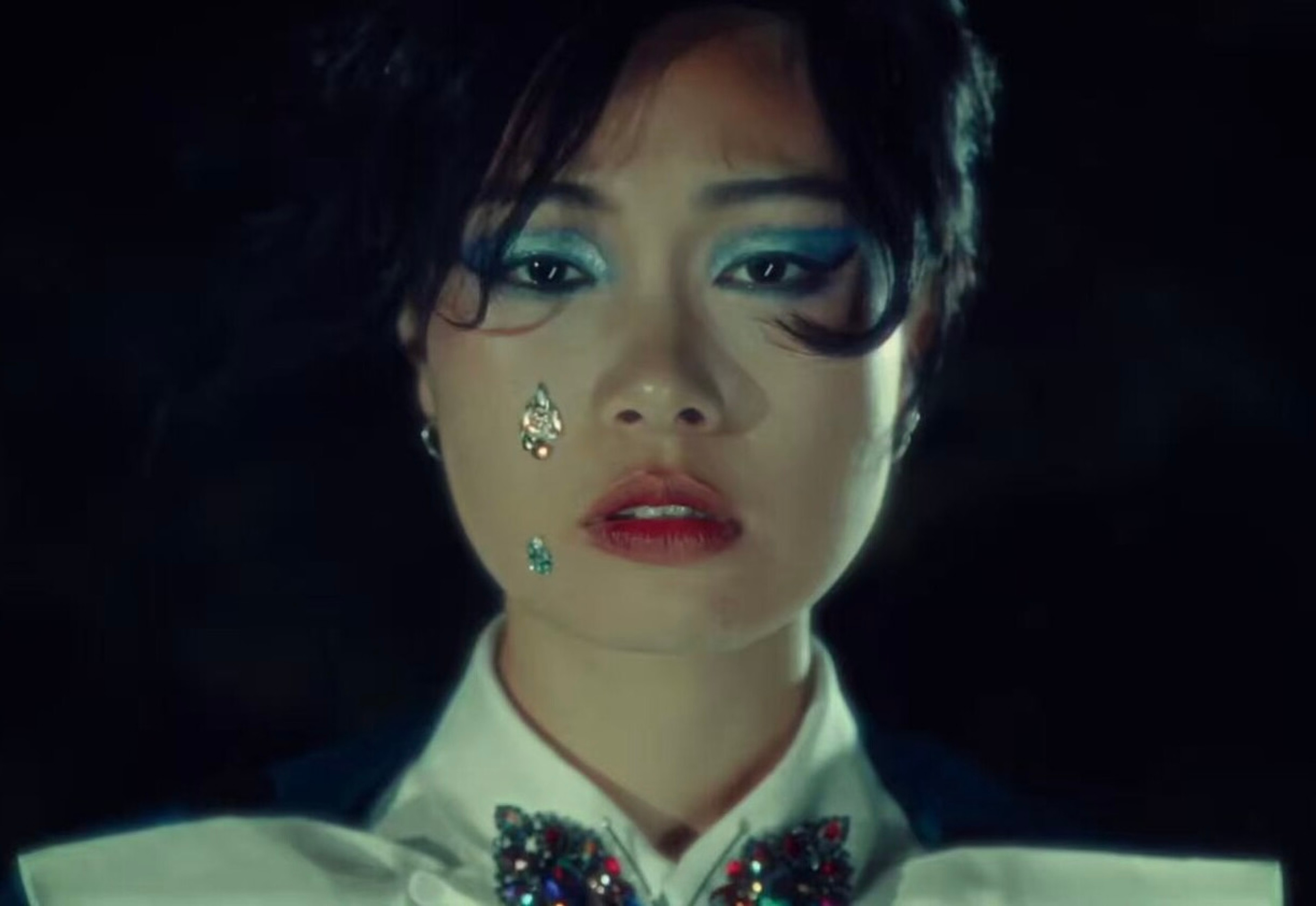 A person's face with blue eye makeup and gem stones.