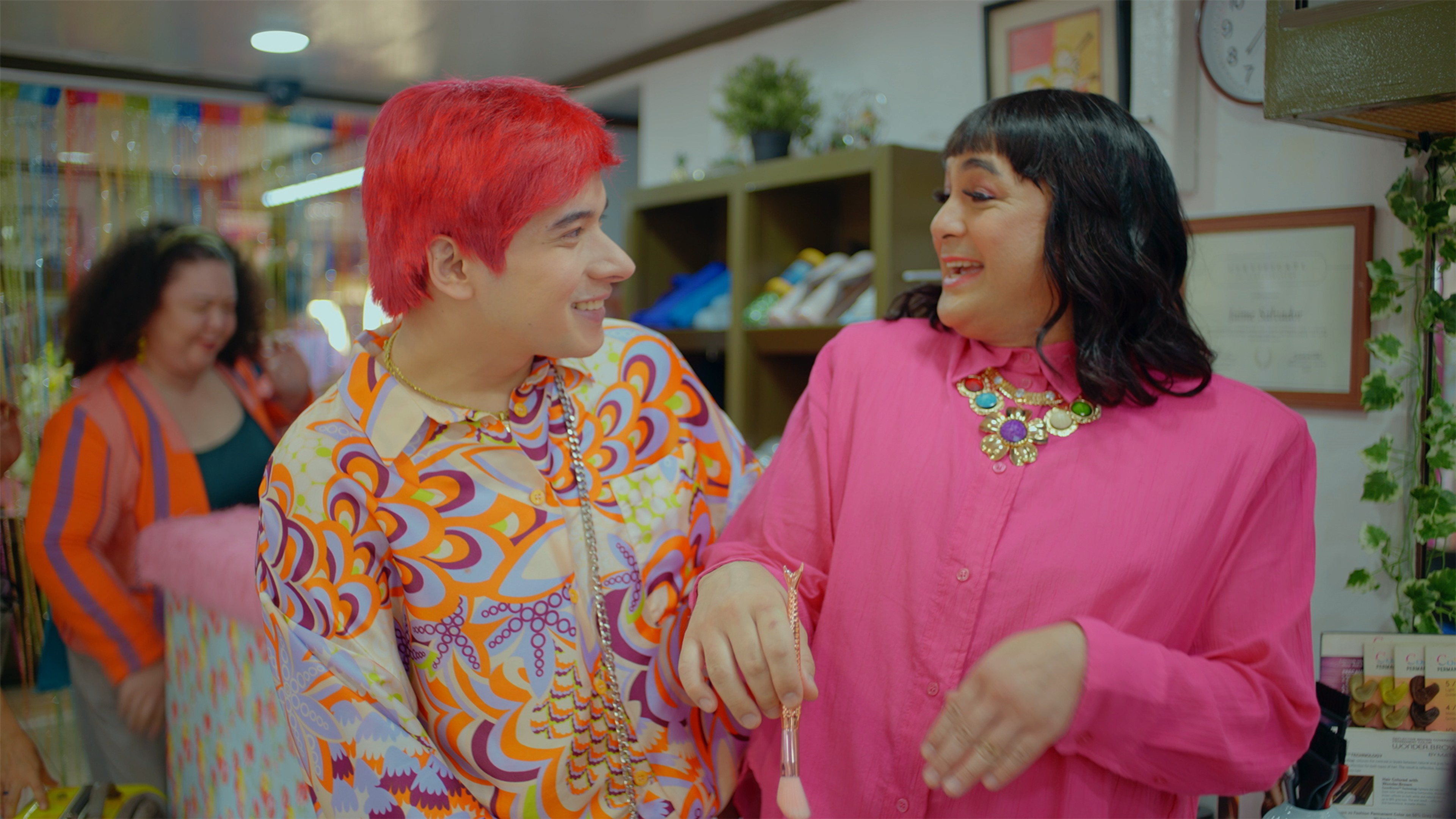 Two people in brightly coloured outfits smiling at each other inside a lively shop.