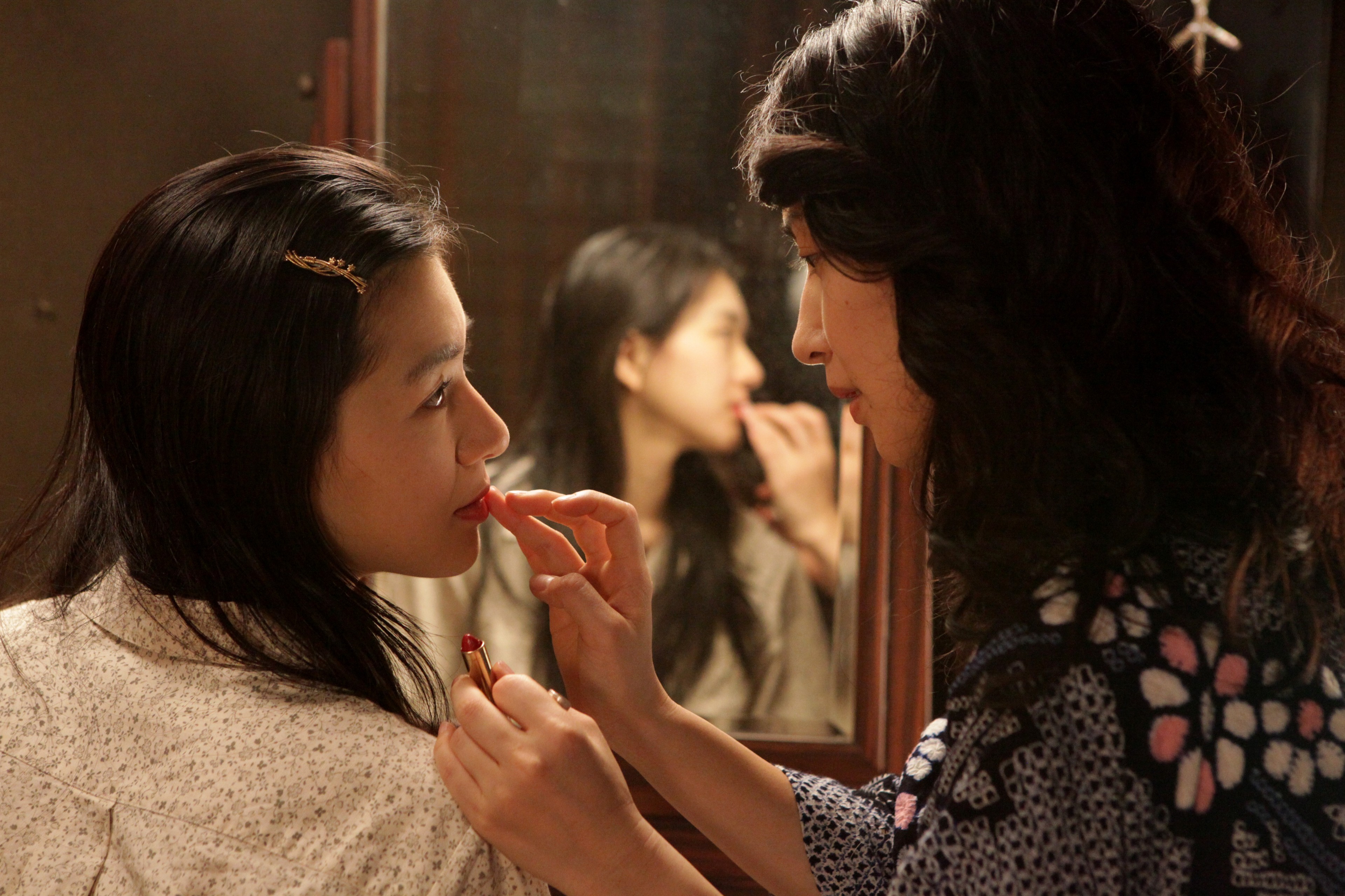 A woman applies lipstick to another woman's lips.