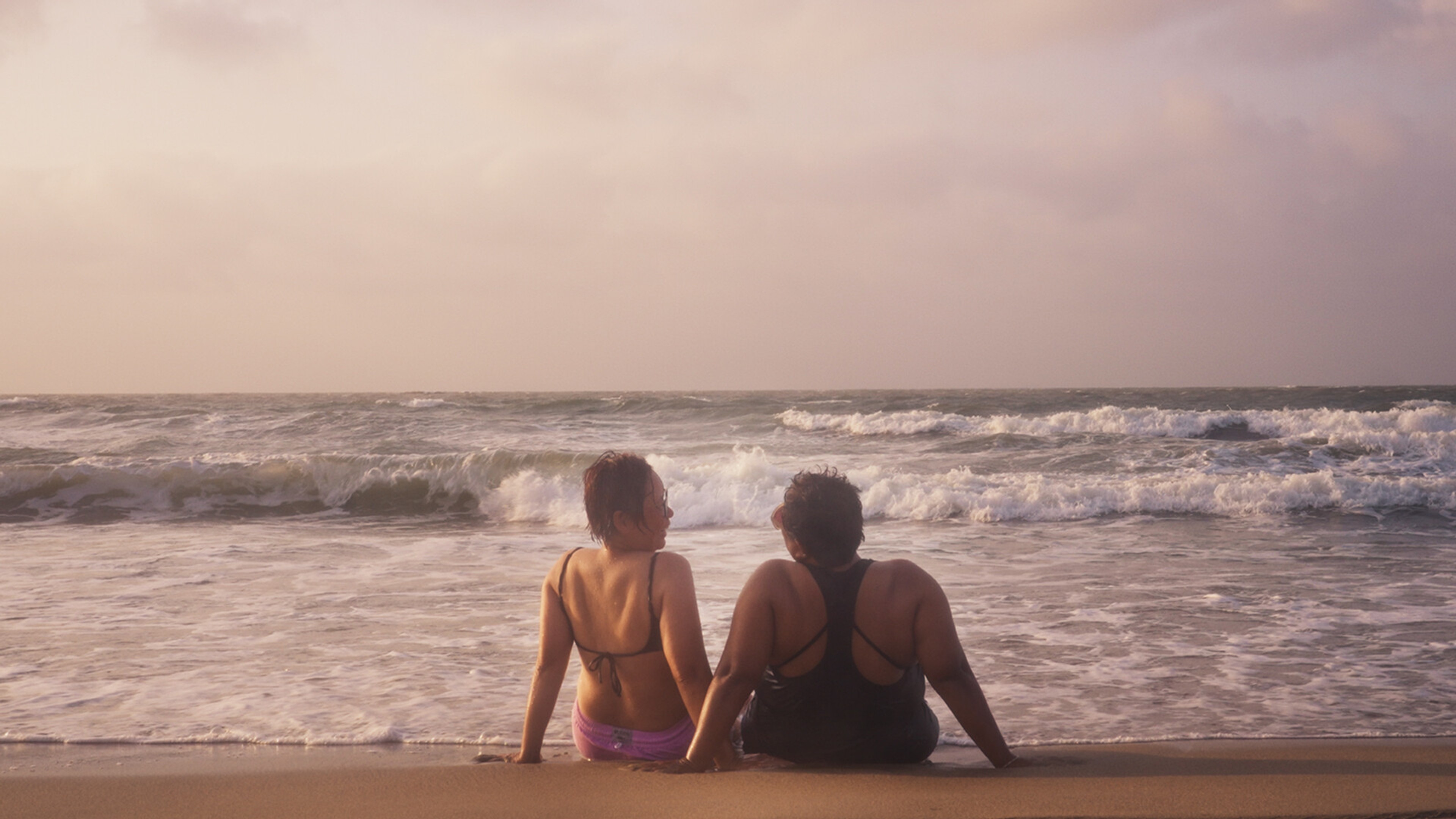Two women sit on a beach.