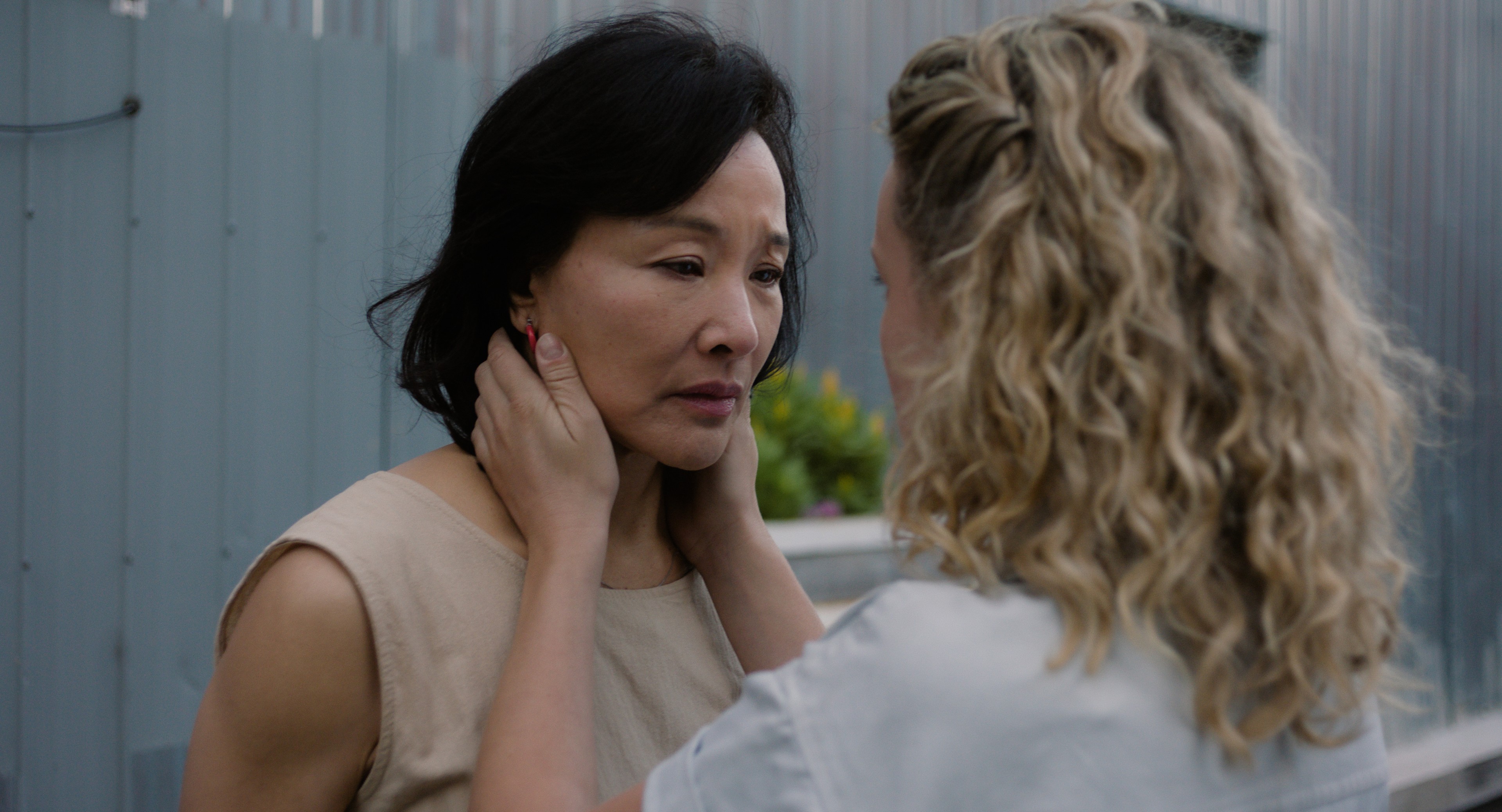 A woman gently holding another woman’s face as they look at each other outdoors.