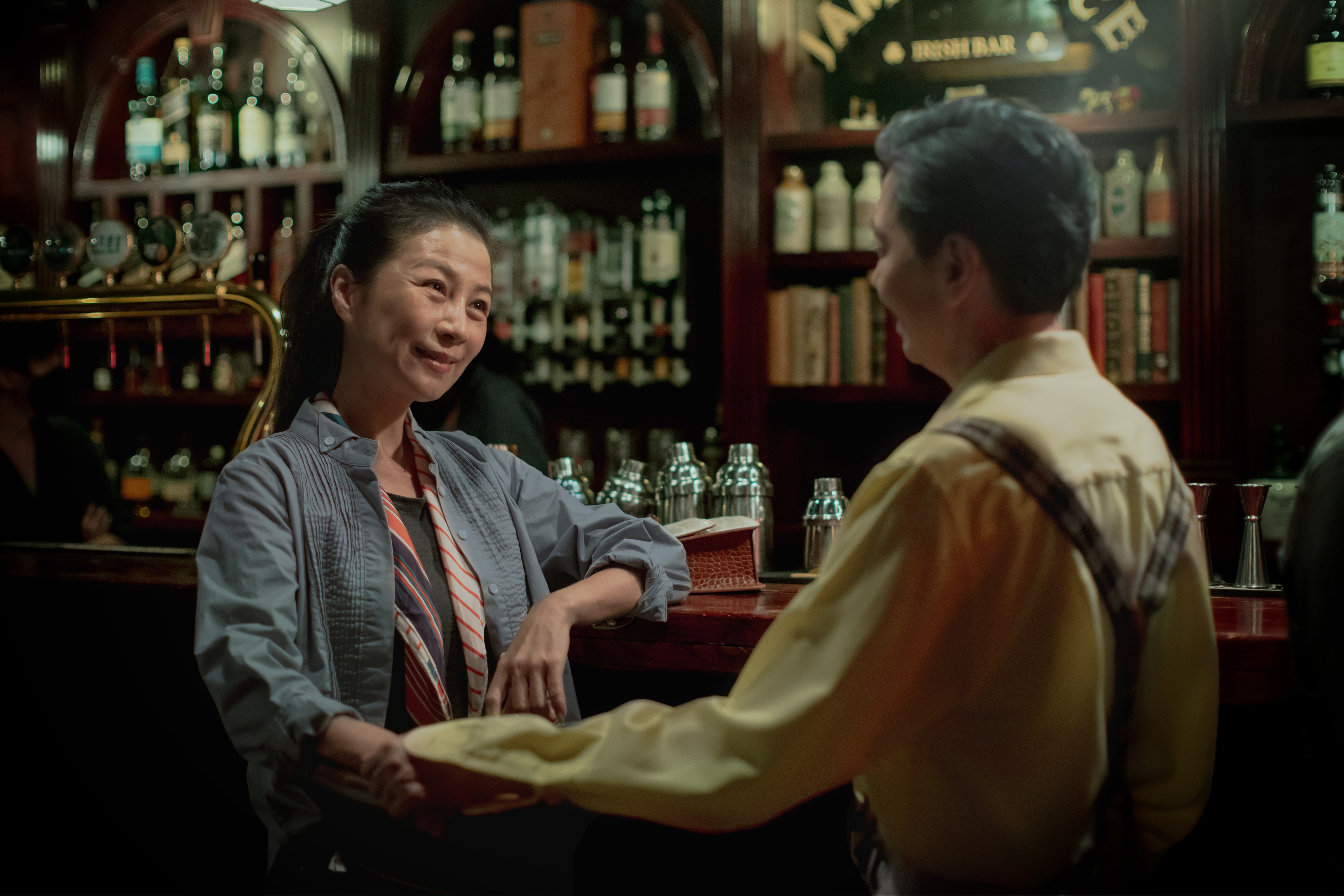 Two people seated closely together at a bar, smiling and holding hands.
