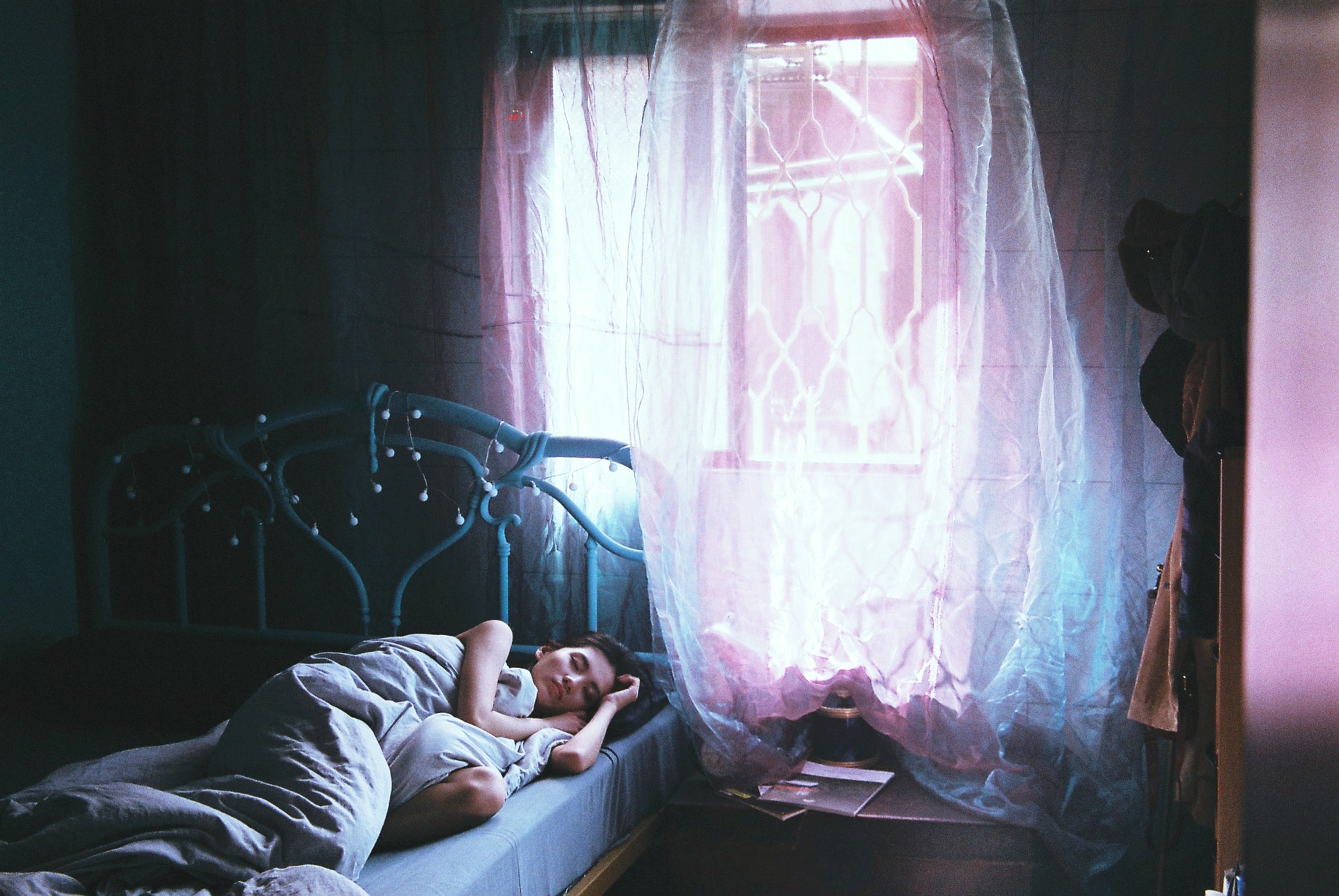 A person lying in bed next to a window emitting pink light.