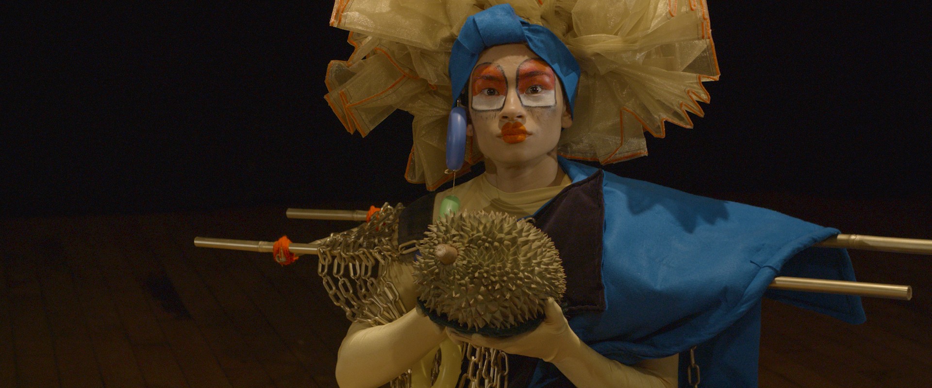 A person wearing a puffy headpiece holds a durian.