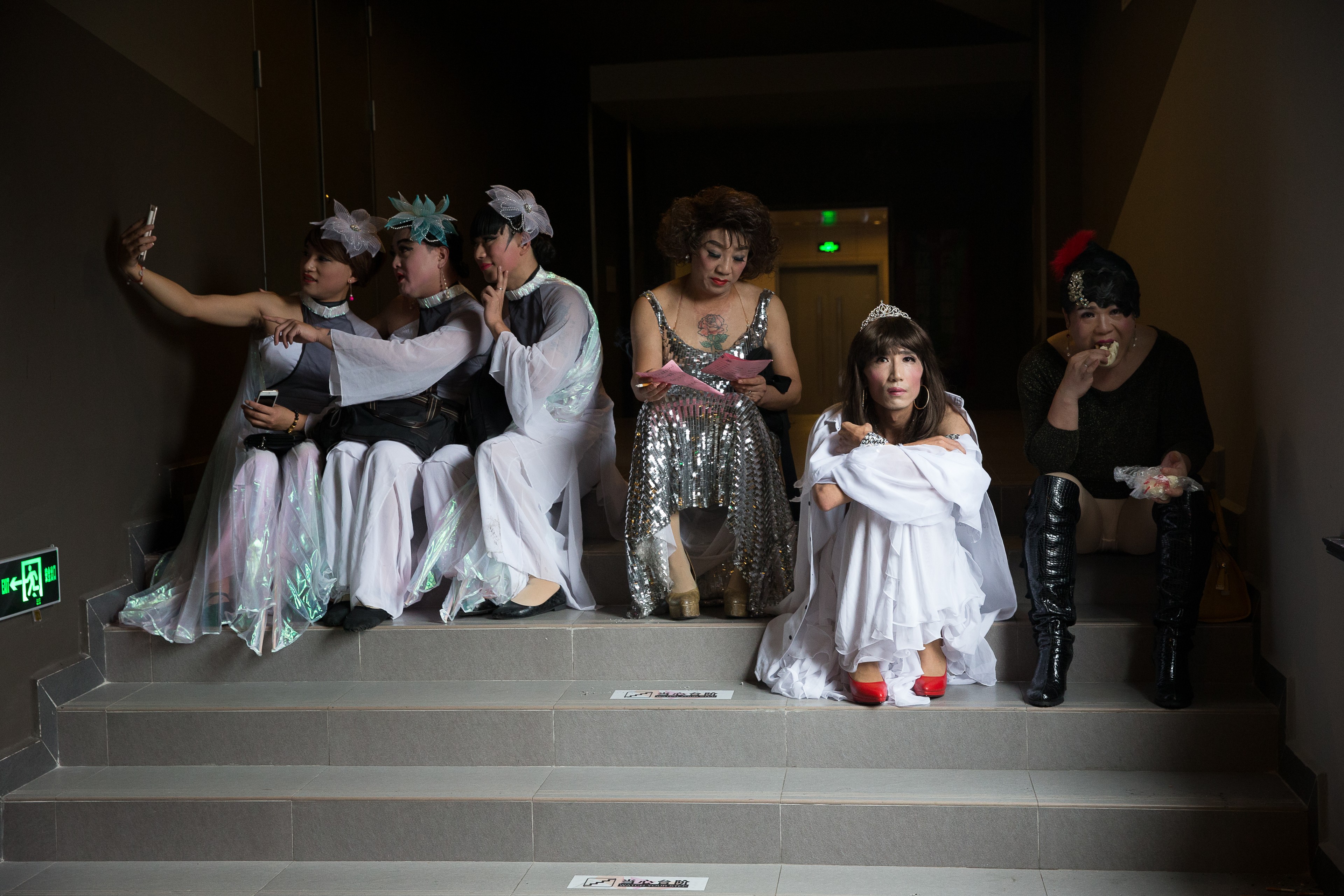 A group of performers in elaborate costumes sitting together on a stairwell backstage.
